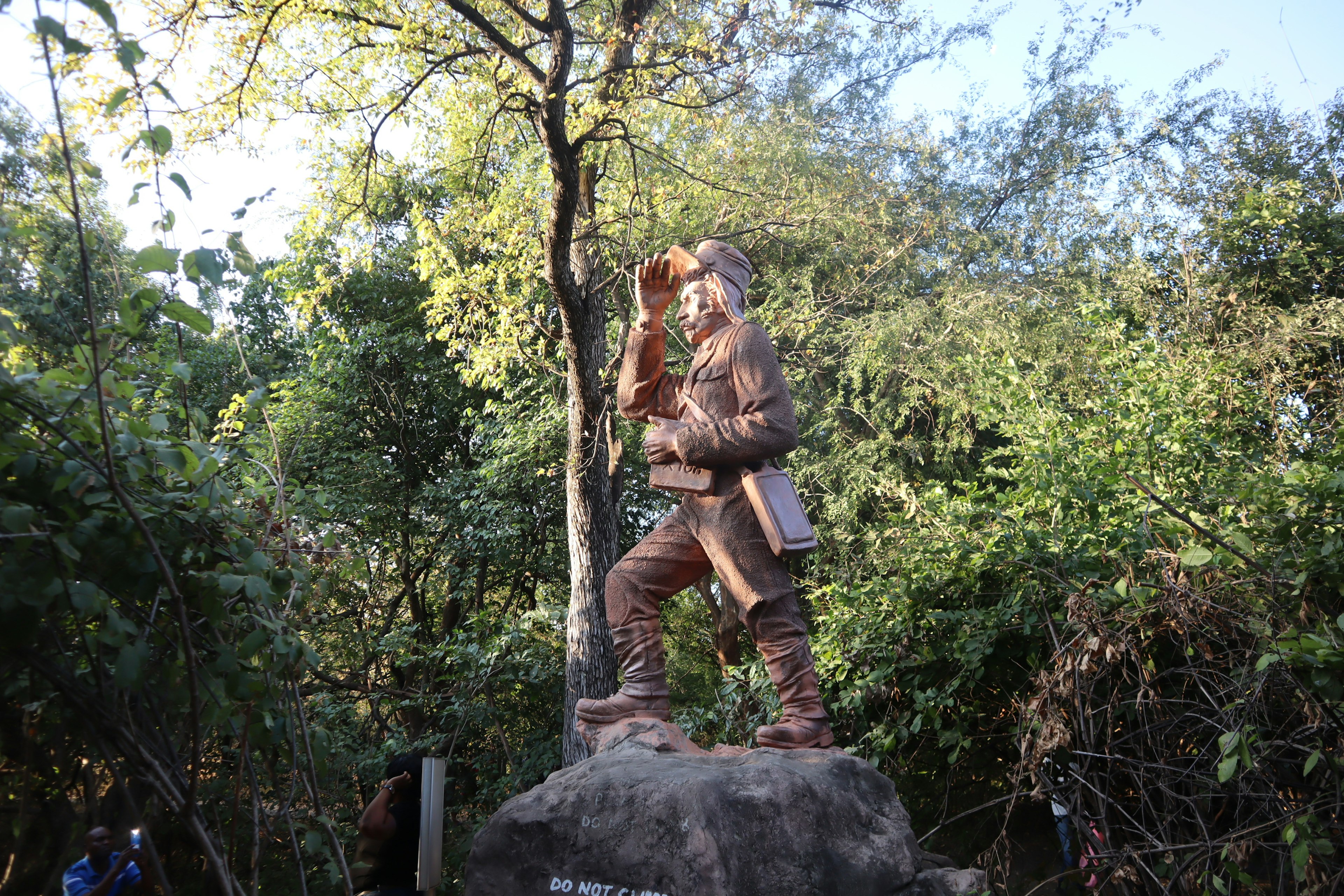 A statue of a man wearing a hat and holding a staff surrounded by greenery