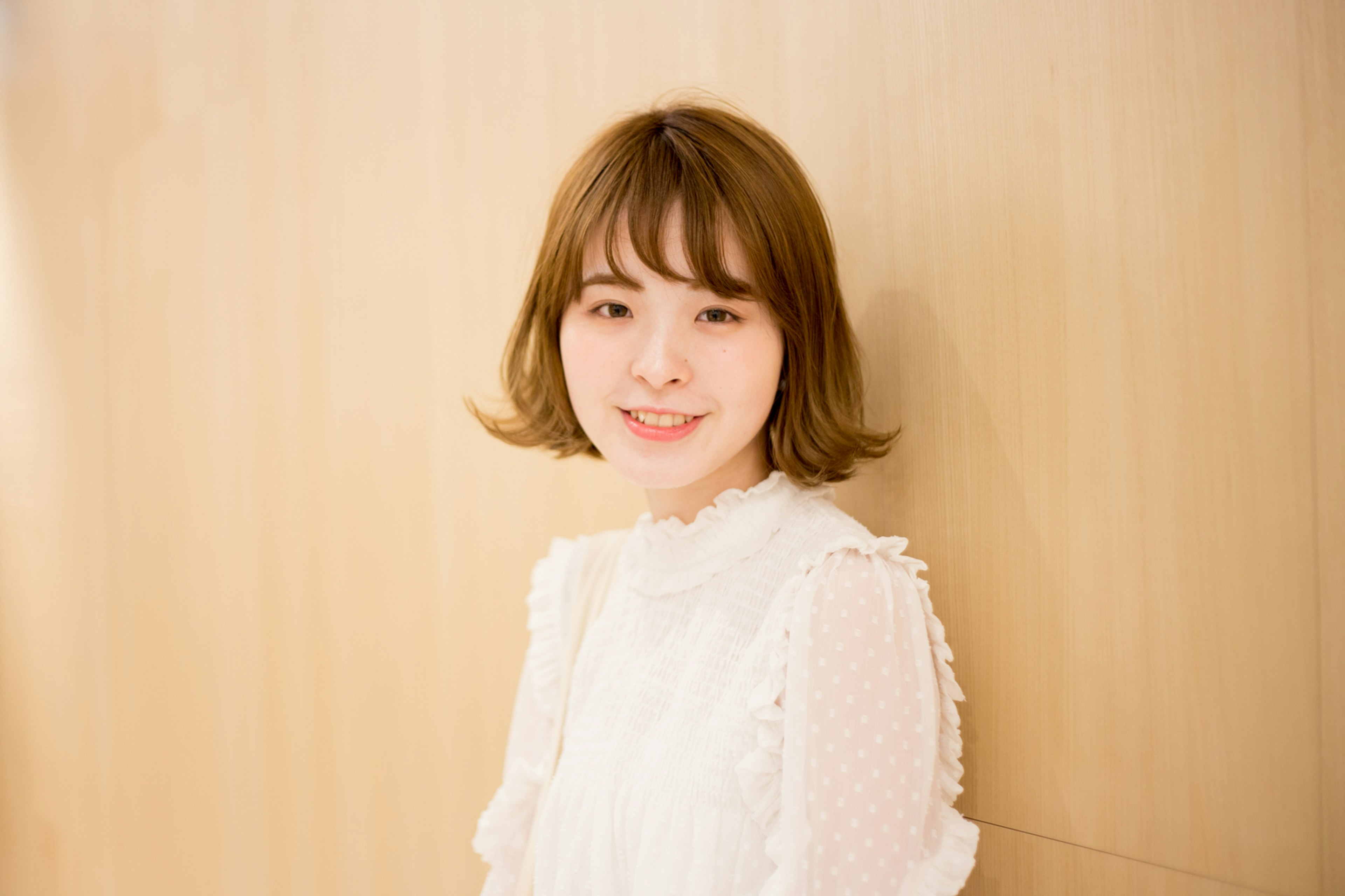 A young woman smiling in a white blouse against a wooden background