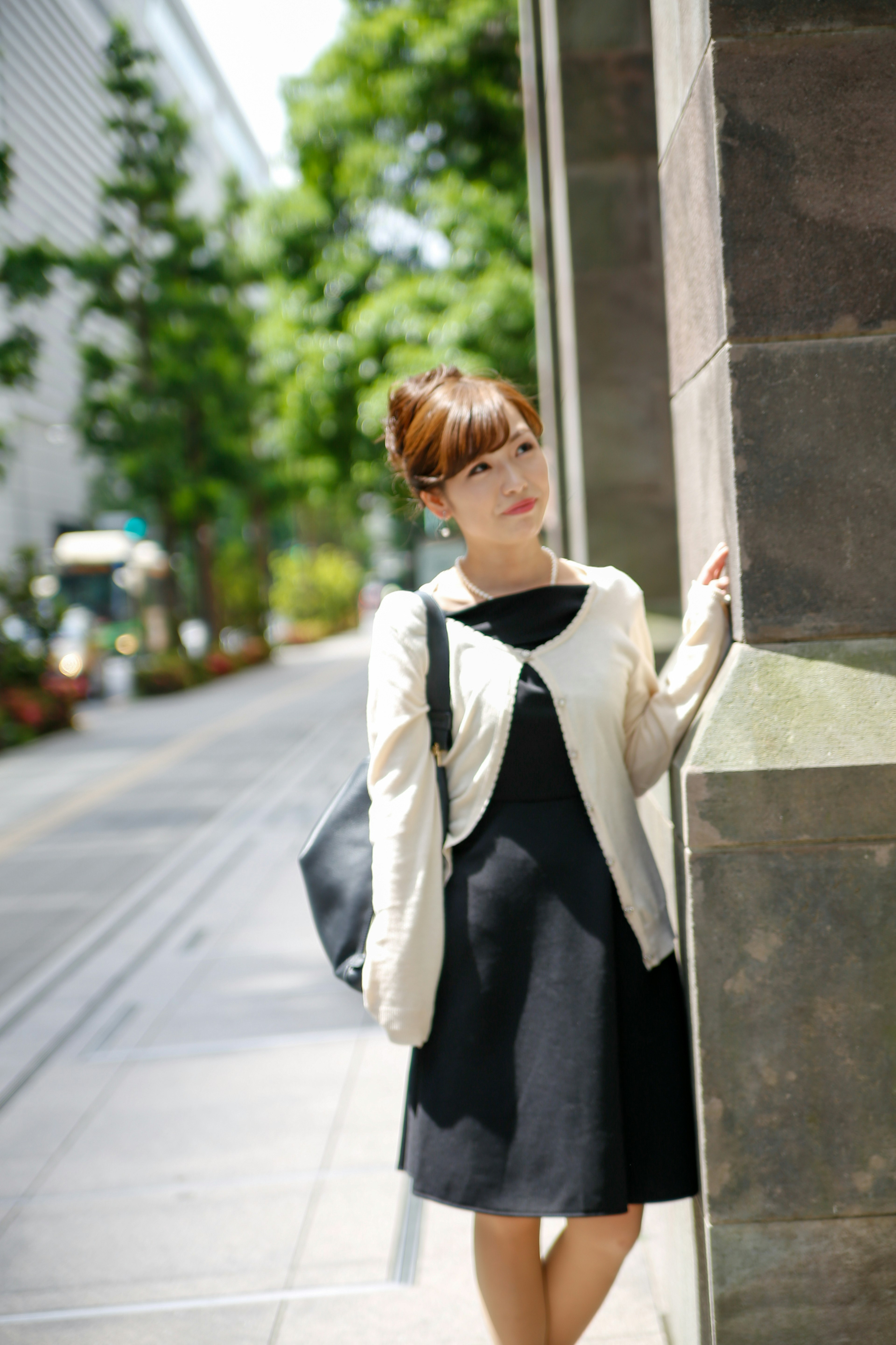 Femme en robe noire et cardigan beige se tenant à un coin de rue