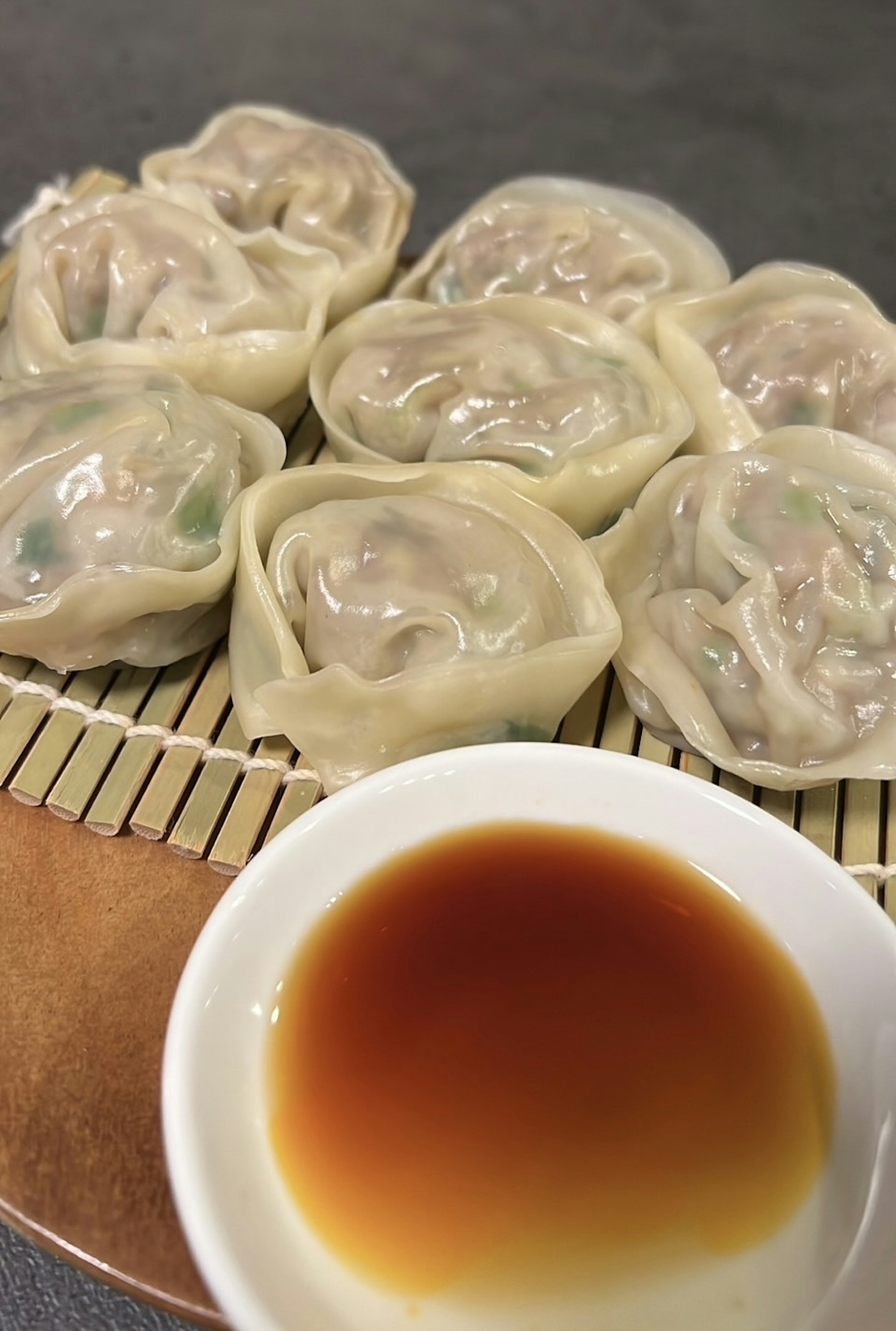 Dumplings al vapor sobre una estera de bambú con un pequeño tazón de salsa de soja