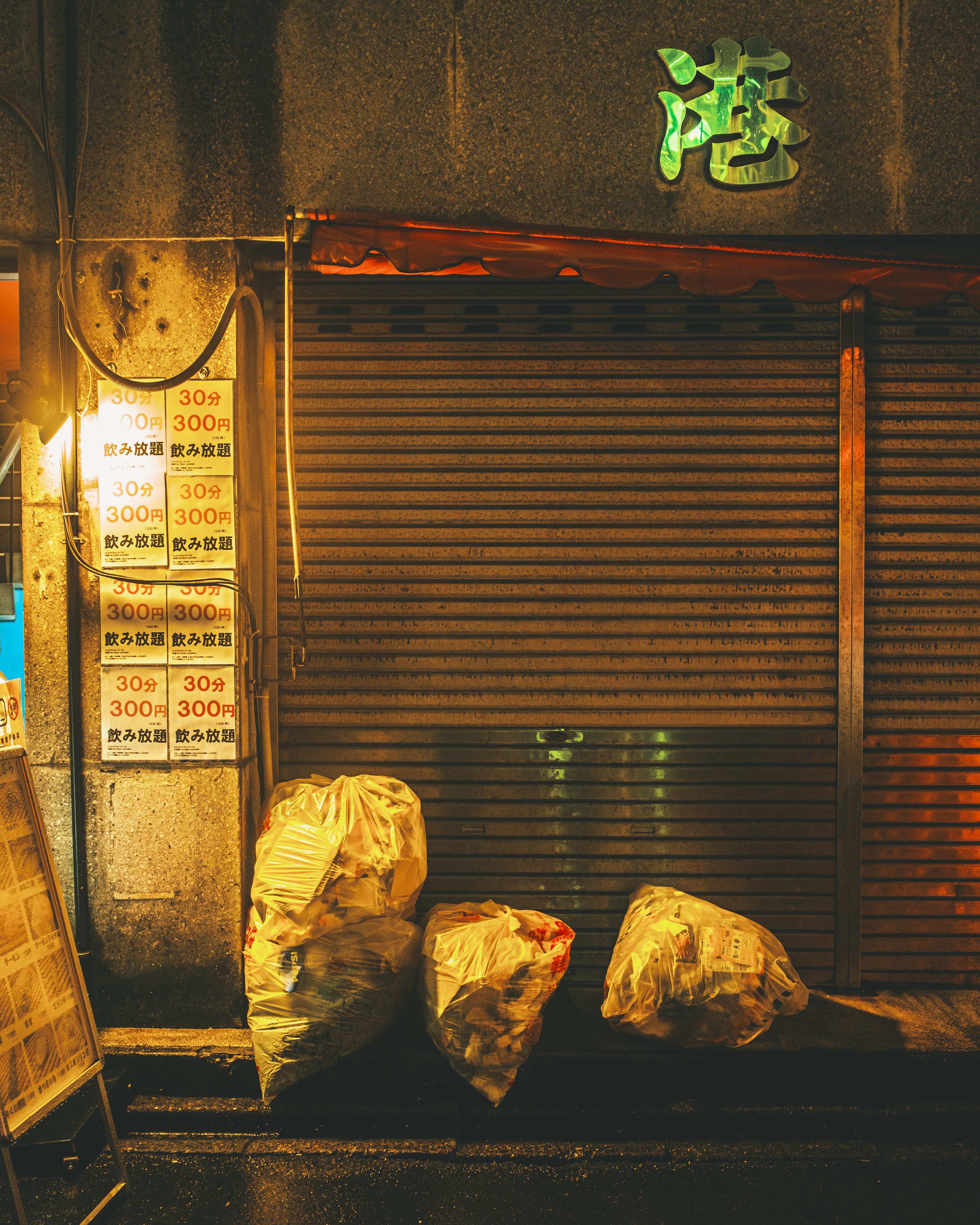 Tienda en un callejón oscuro con un letrero verde y grandes bolsas de basura delante