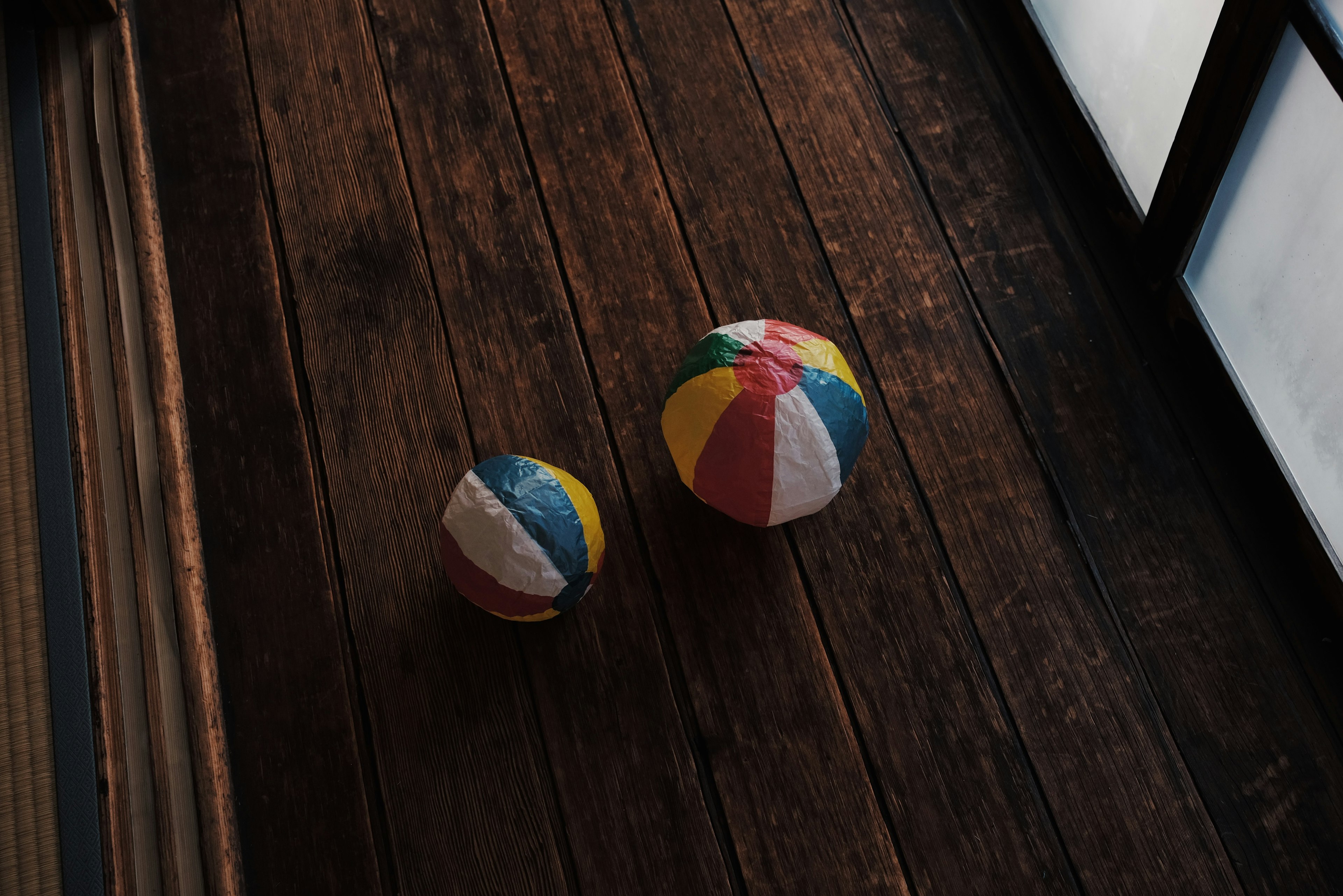 Two colorful beach balls on a wooden floor