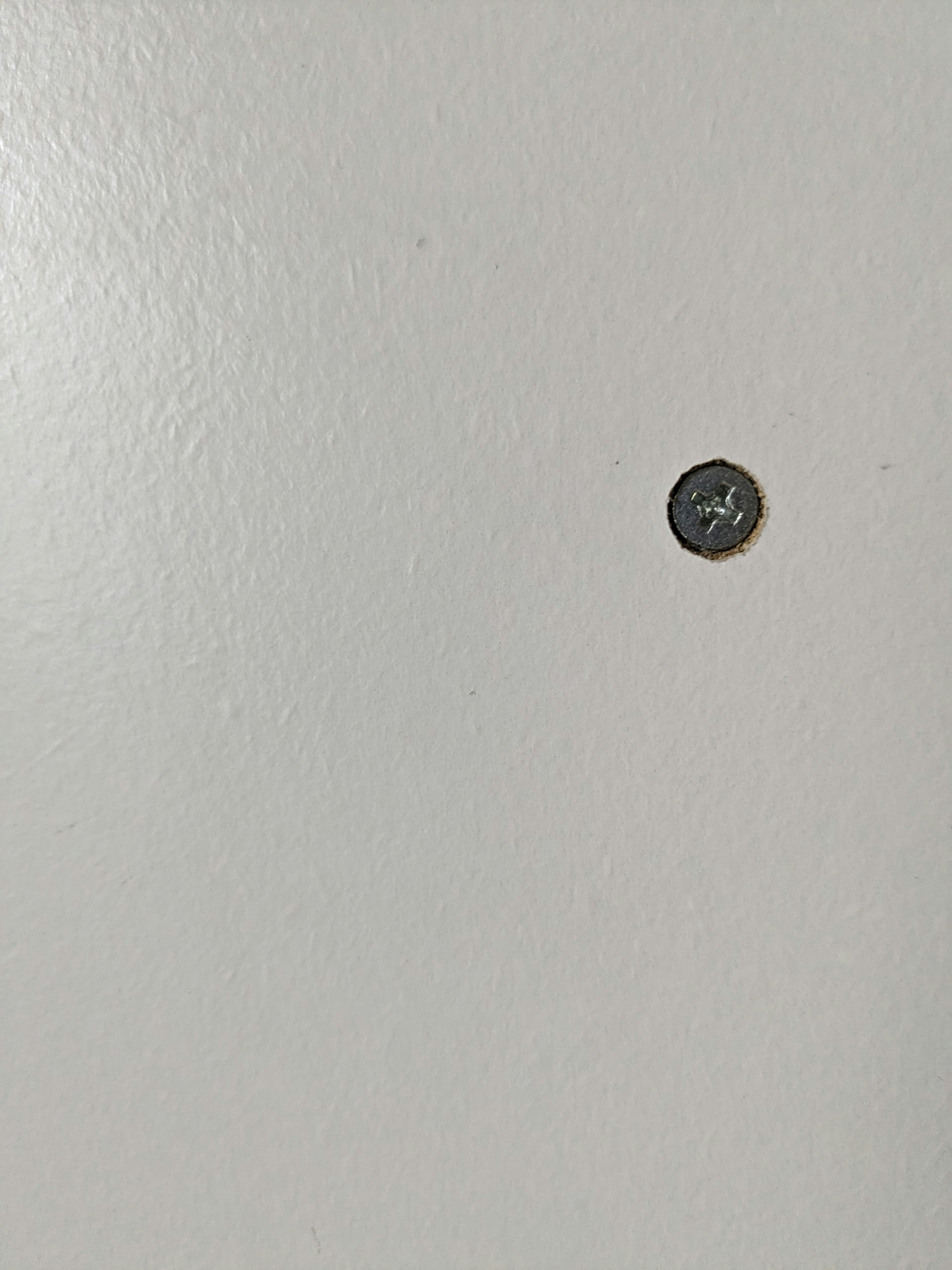 Une image simple d'une vis noire sur un mur blanc