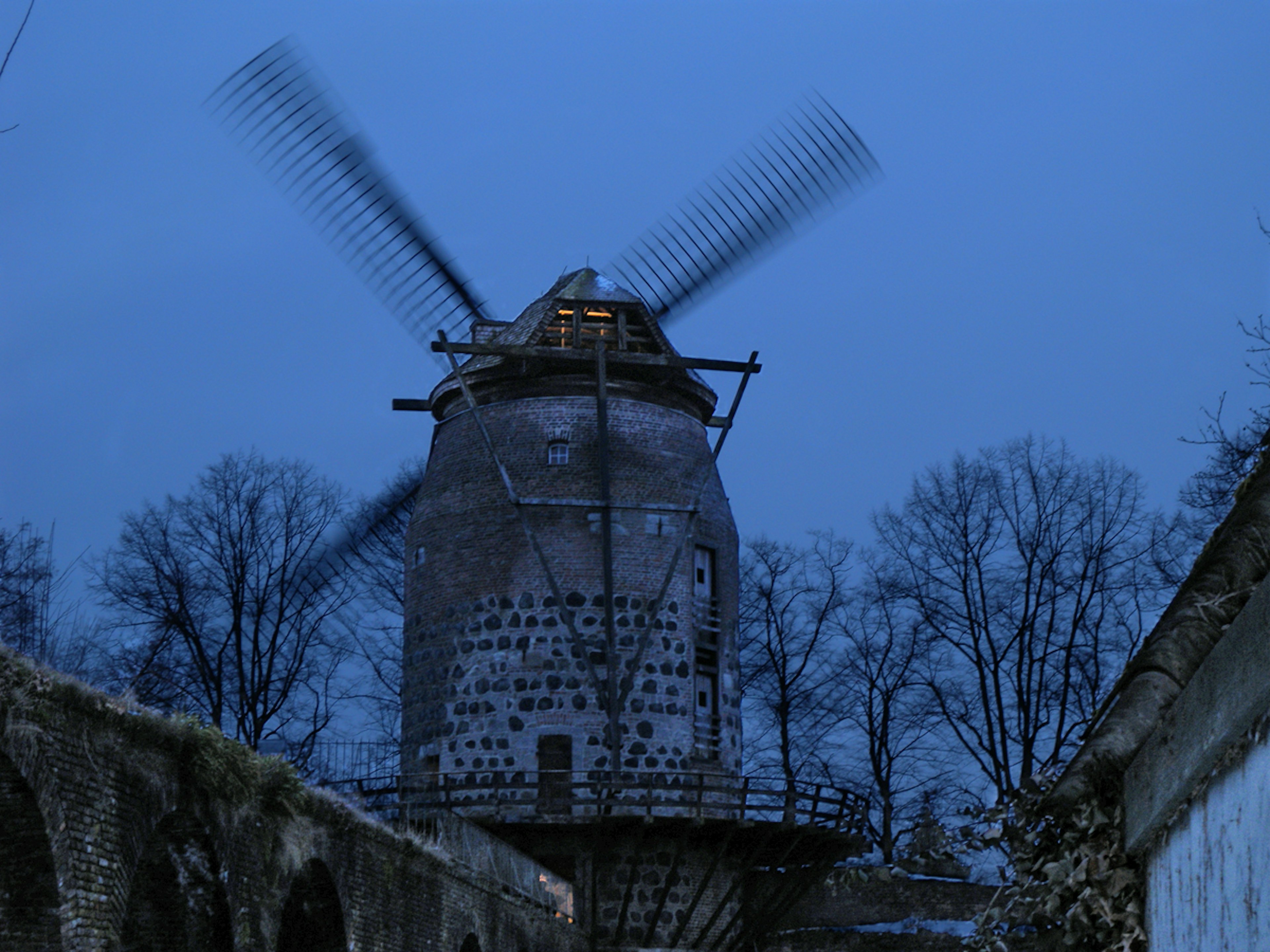 Imagen de un molino de viento girando contra un cielo nocturno azul con árboles alrededor