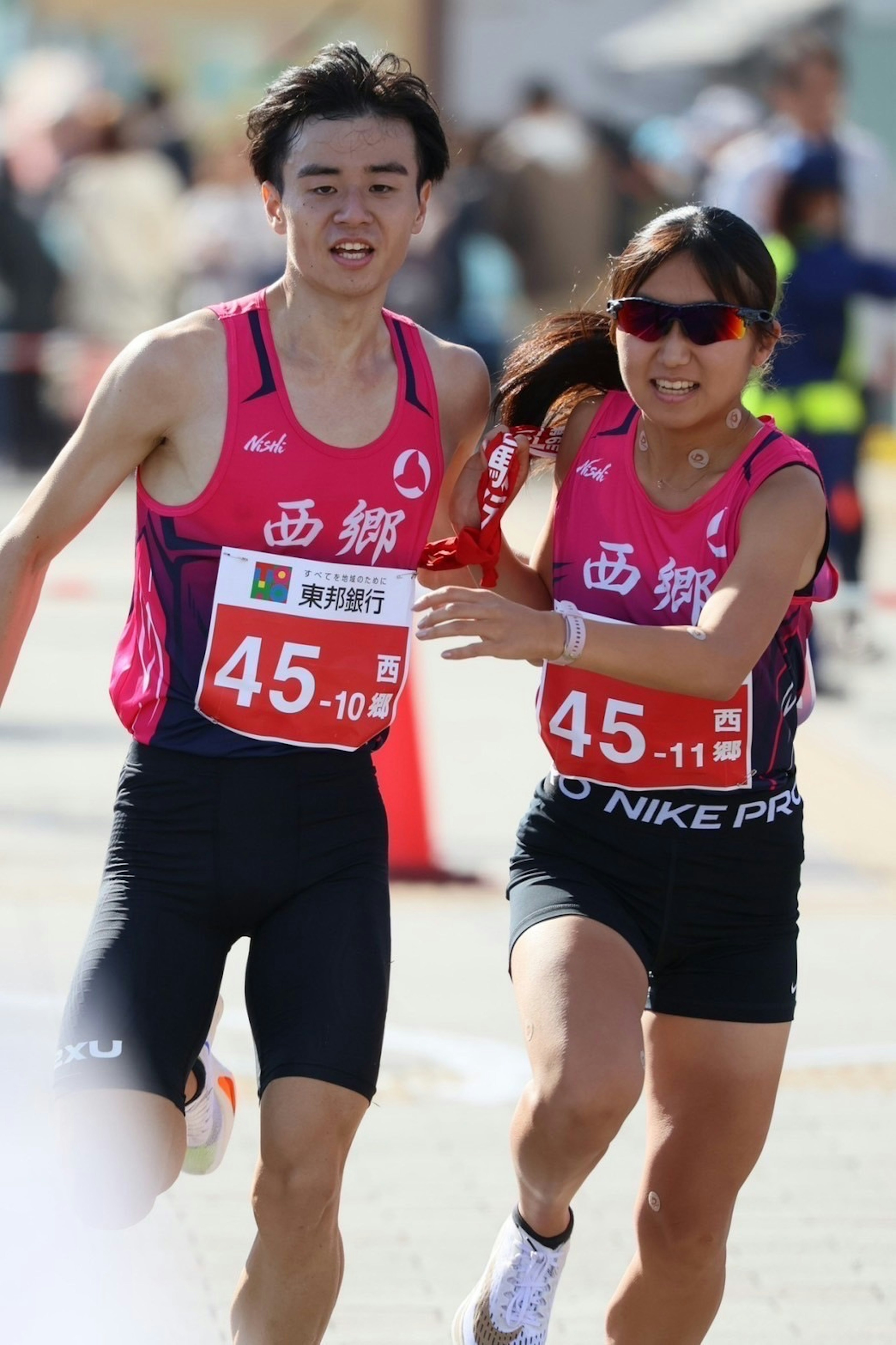 Two runners exchanging a baton in a relay race wearing pink uniforms with spectators in the background