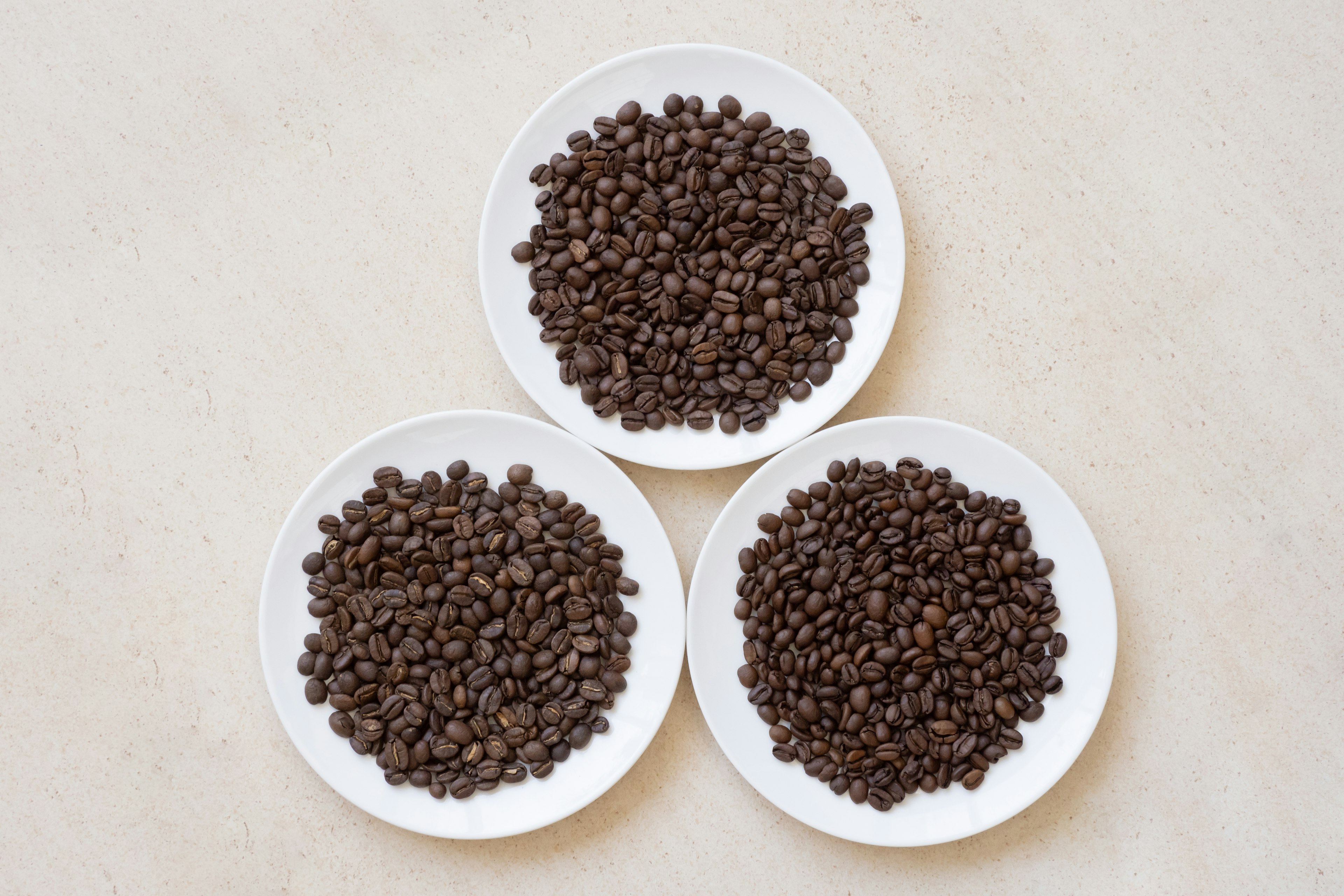 Three white plates filled with coffee beans arranged in a triangular formation