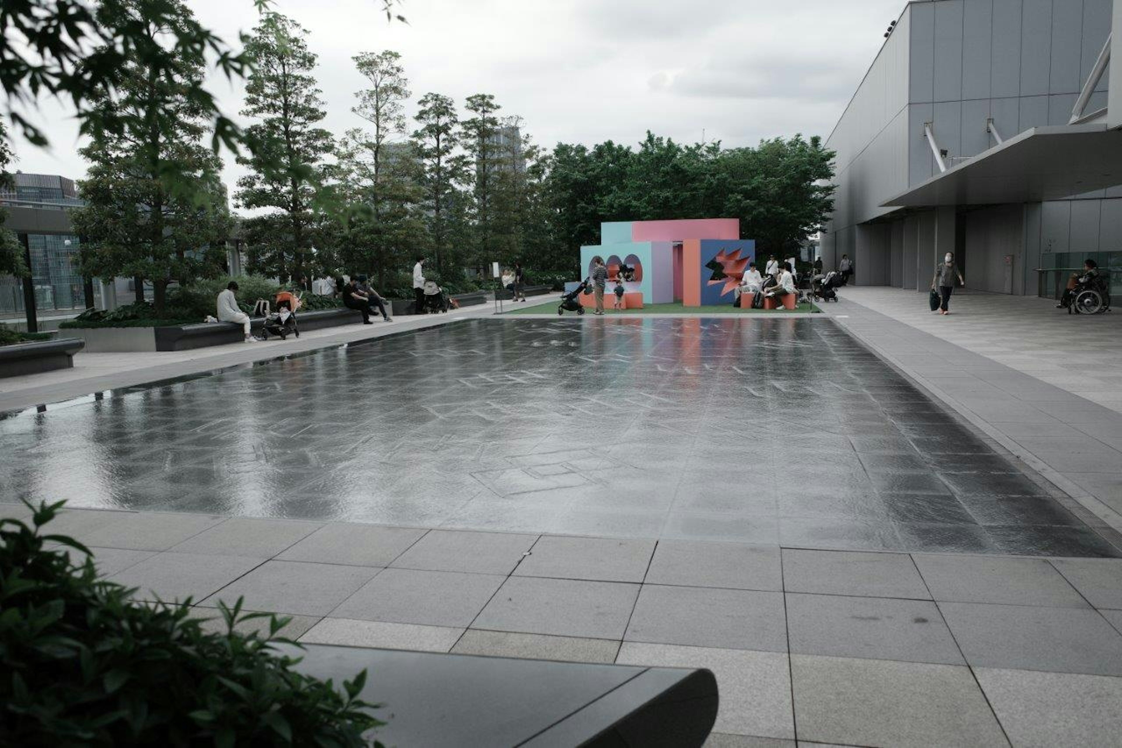 Una escena de parque tranquila con una piscina reflectante y una instalación artística colorida