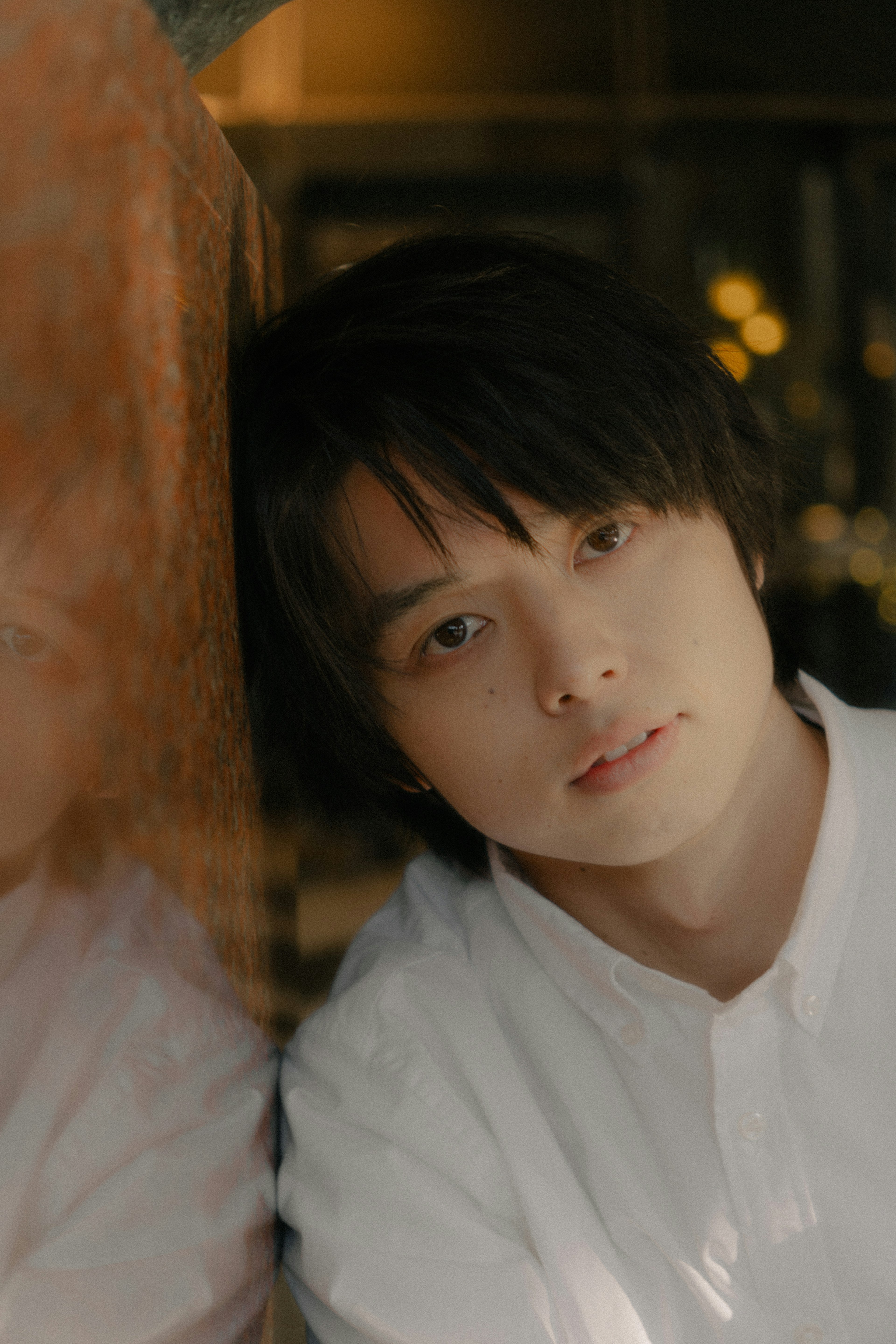 A young man leaning against a wall with a gentle smile