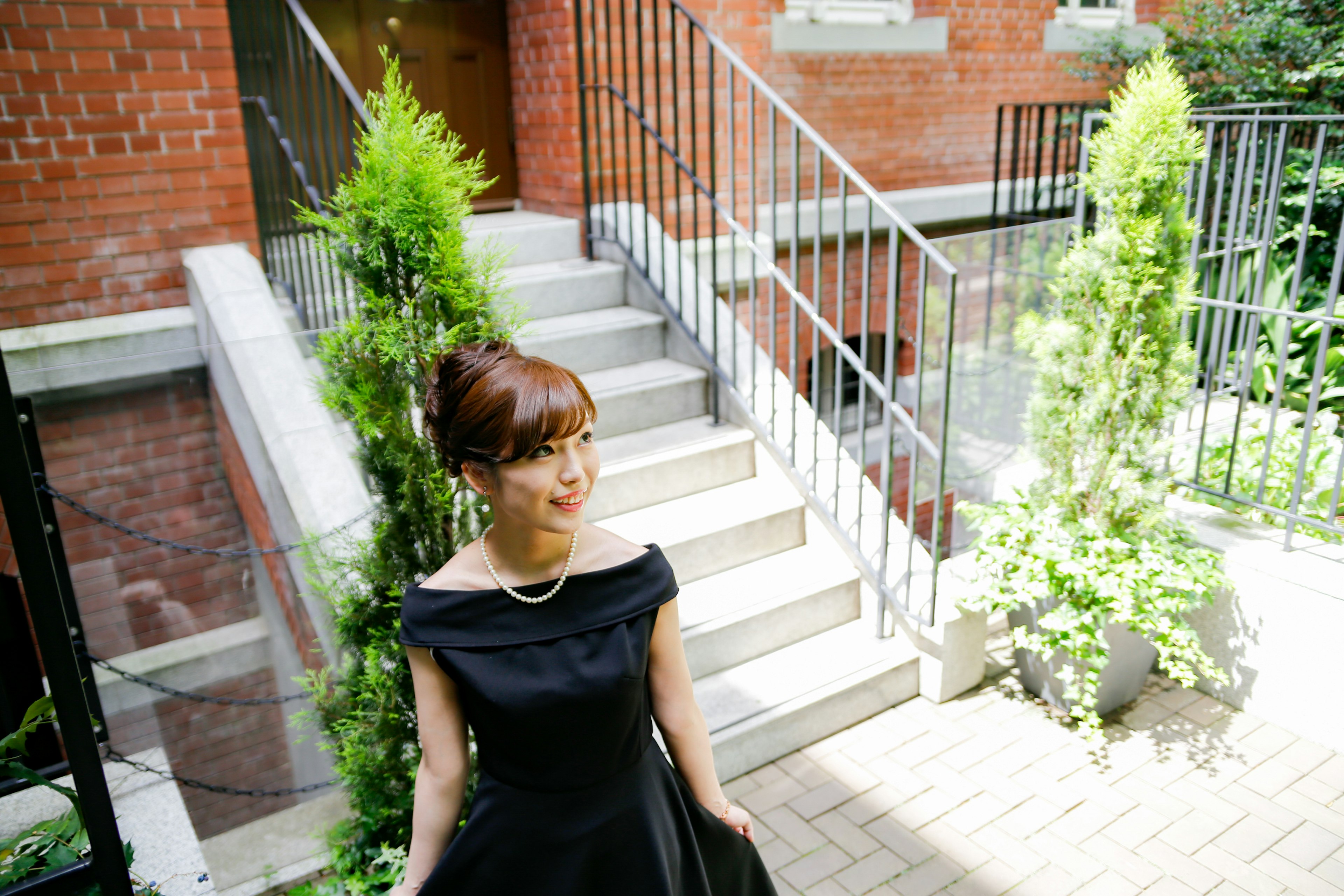 Woman in a black dress smiling near green plants