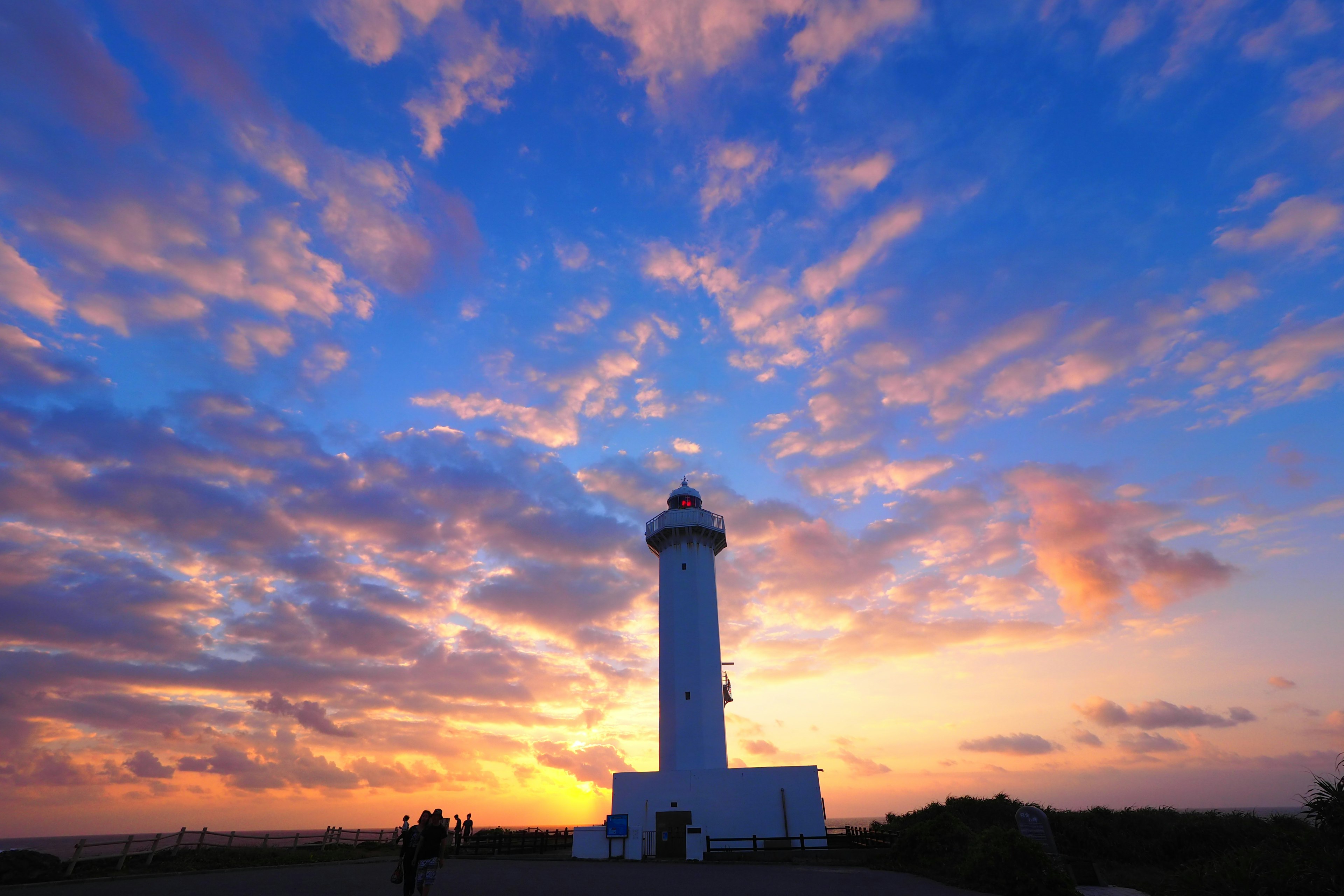 青い空とオレンジ色の夕焼けの中に立つ白い灯台