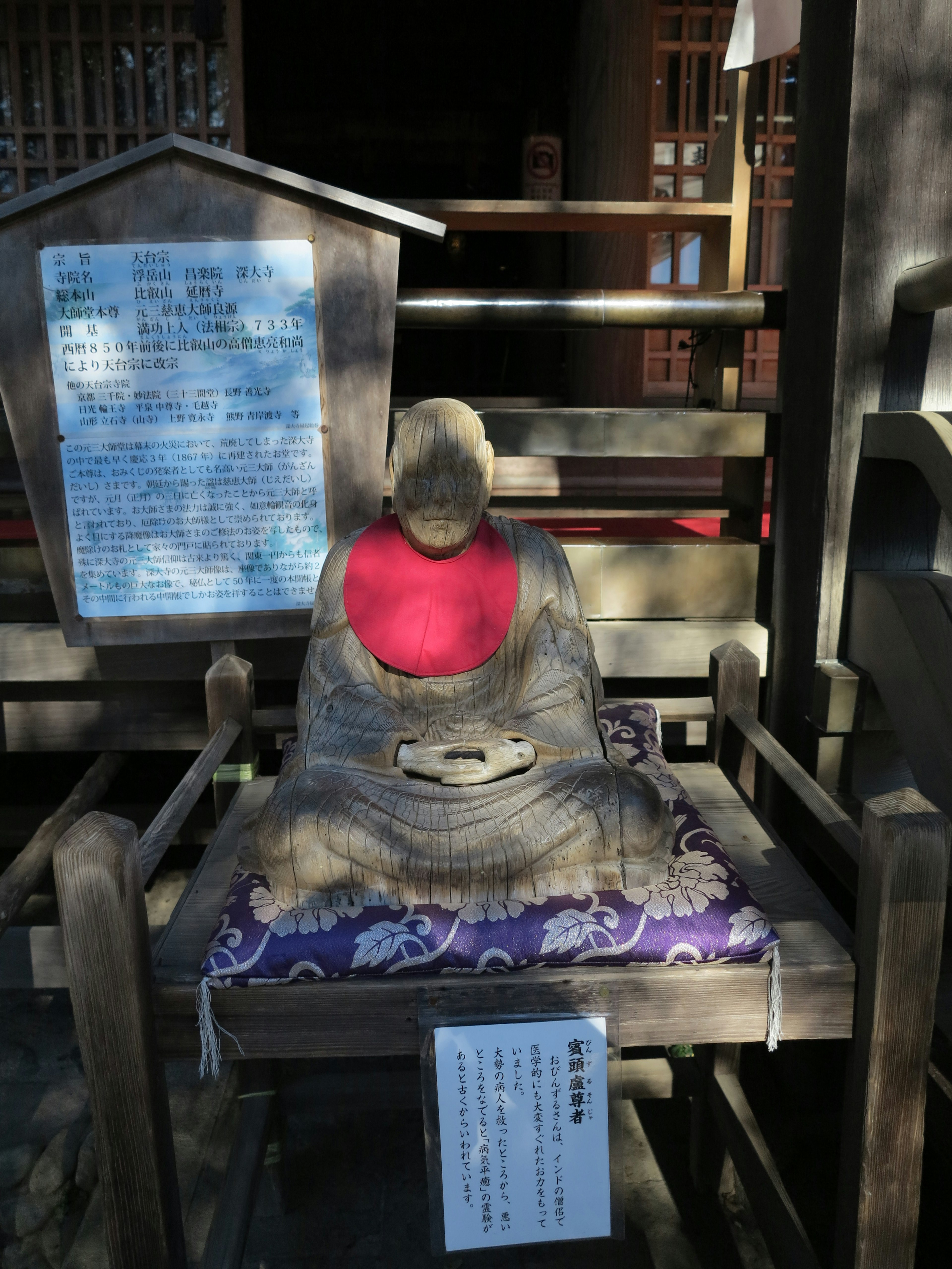 A seated statue of a Buddha wearing a red garment on a wooden pedestal