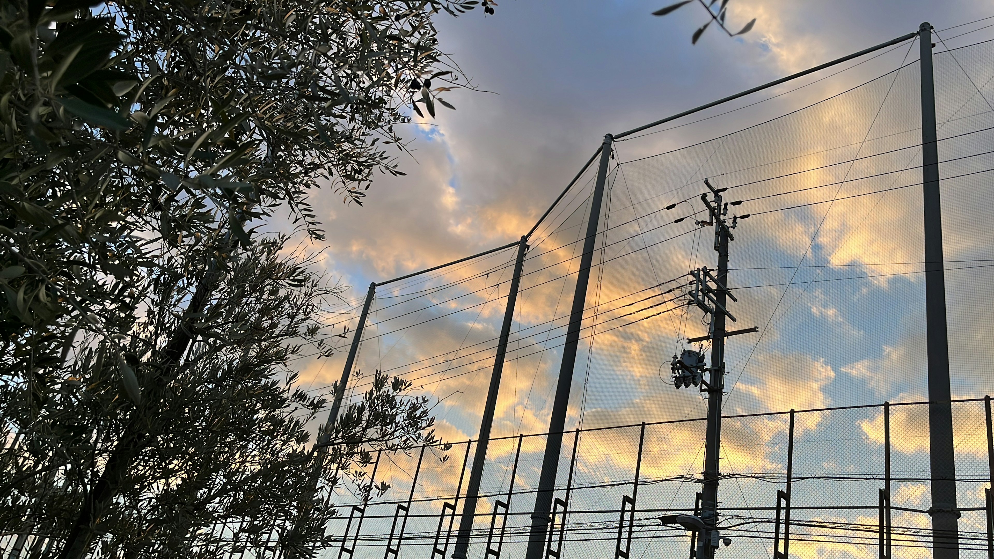 空に広がる雲と電柱のシルエットを背景にしたネットの構造