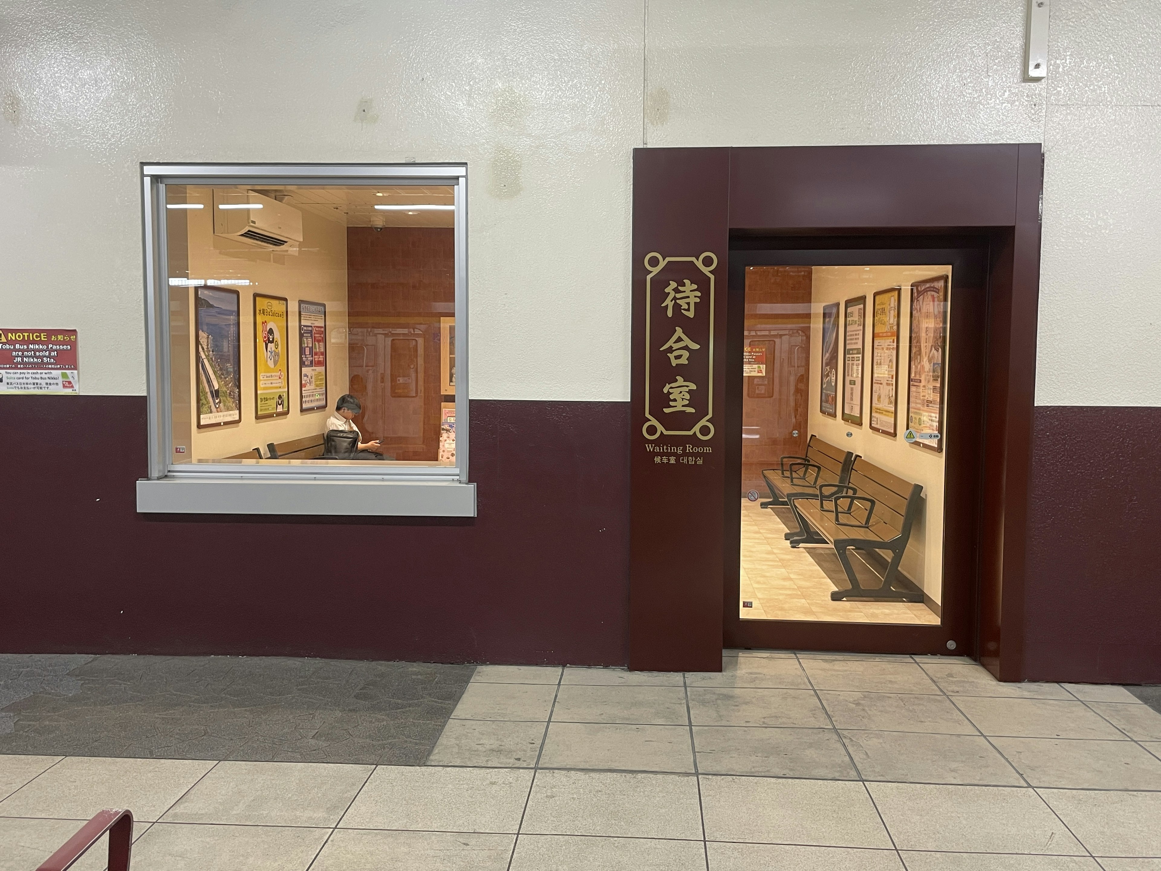 Exterior view of a waiting area with a window and door featuring numerous posters on the wall