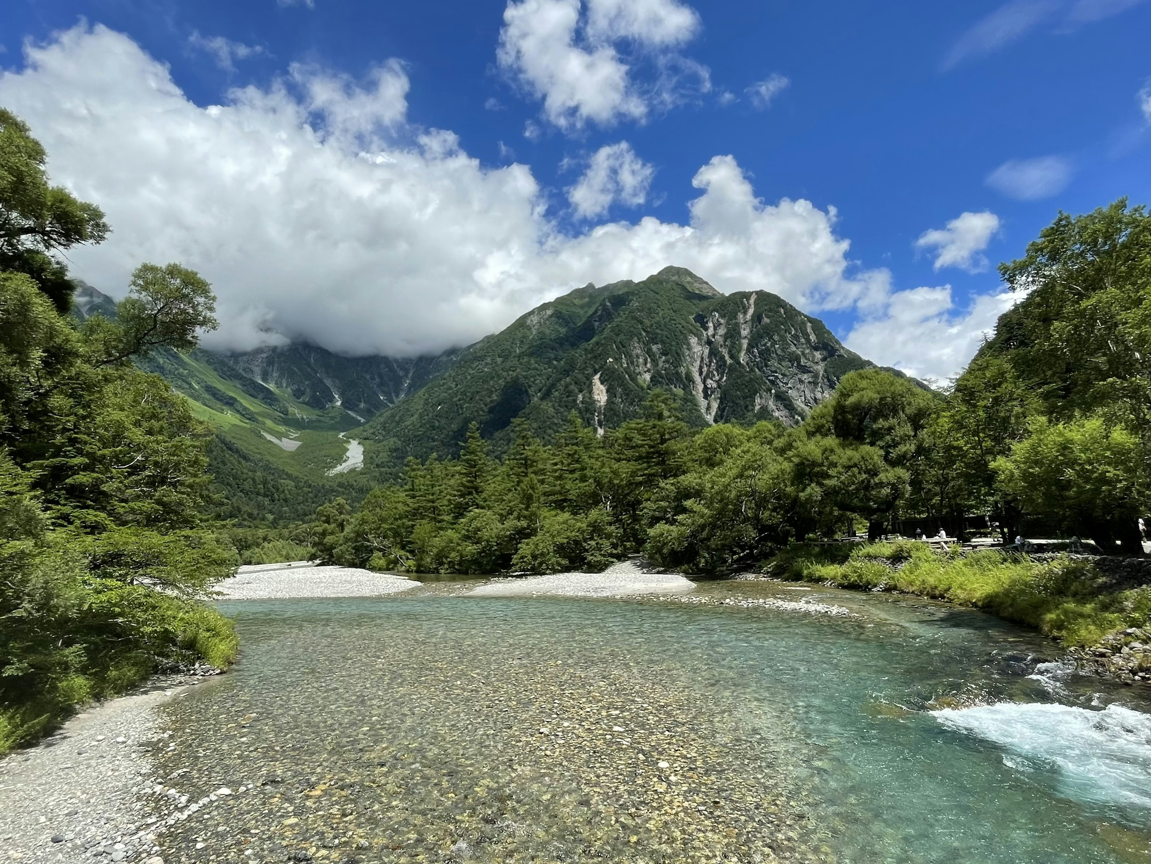 Scenic view of a clear river flowing under lush green mountains and a blue sky