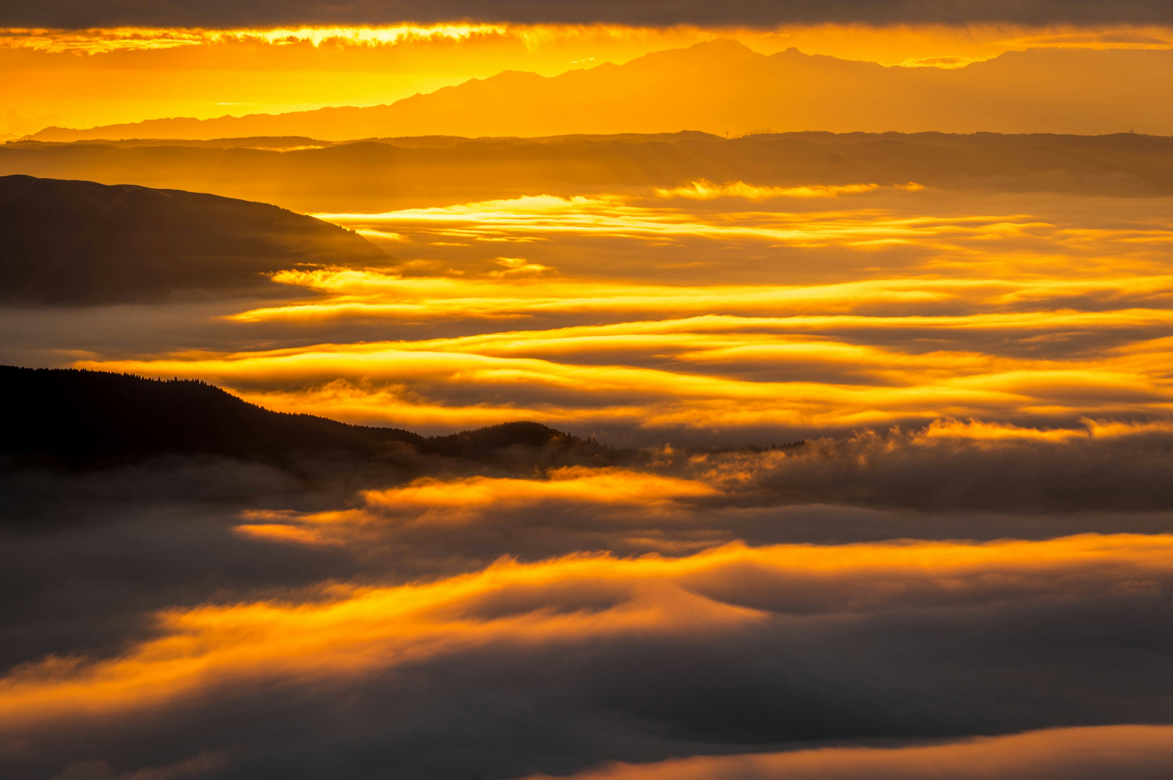 Ein atemberaubender Sonnenuntergang über einem Wolkenmeer mit orangefarbenem Licht, das die Berge beleuchtet