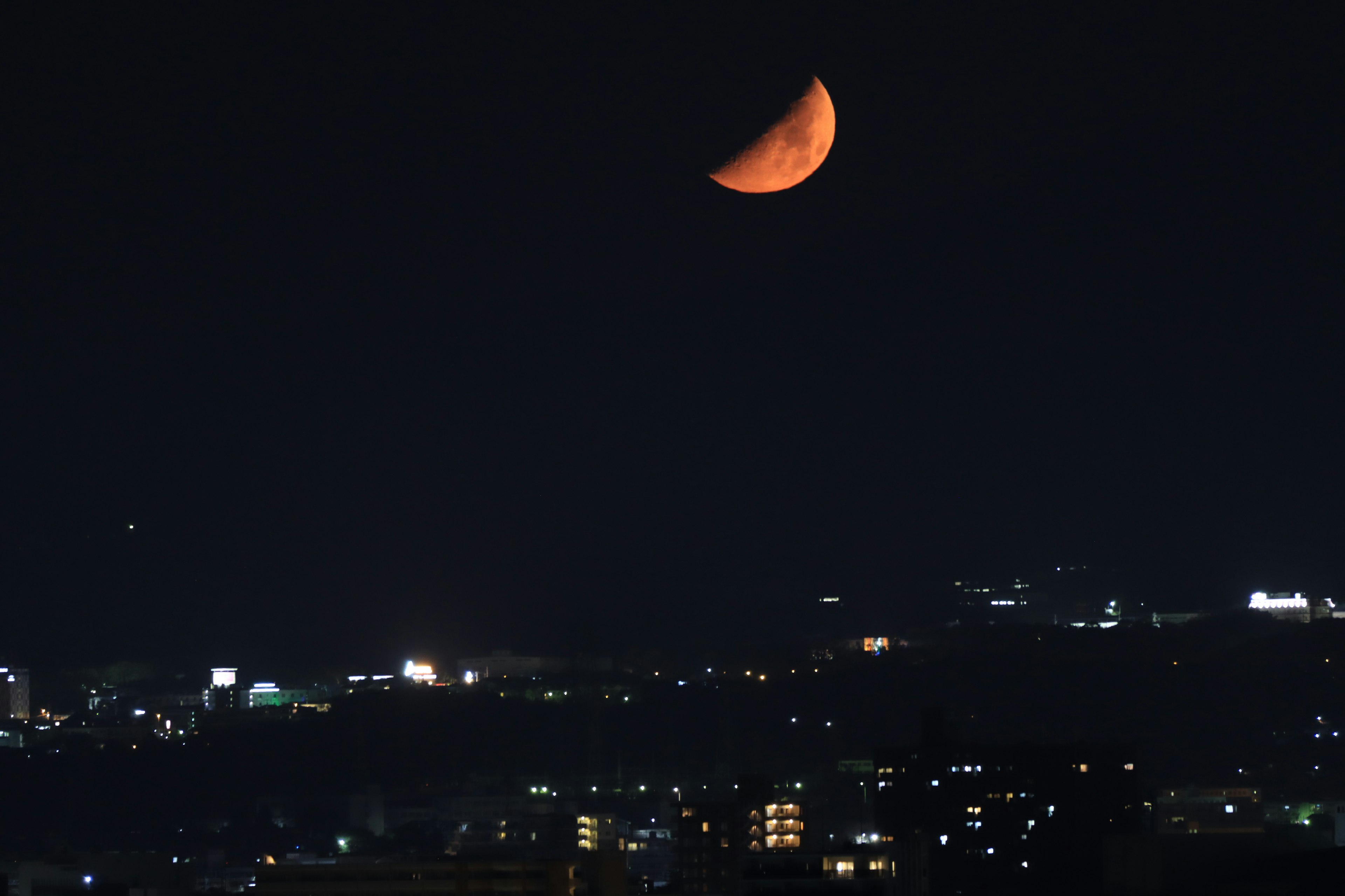 Una luna rossa nel cielo notturno sopra le luci della città