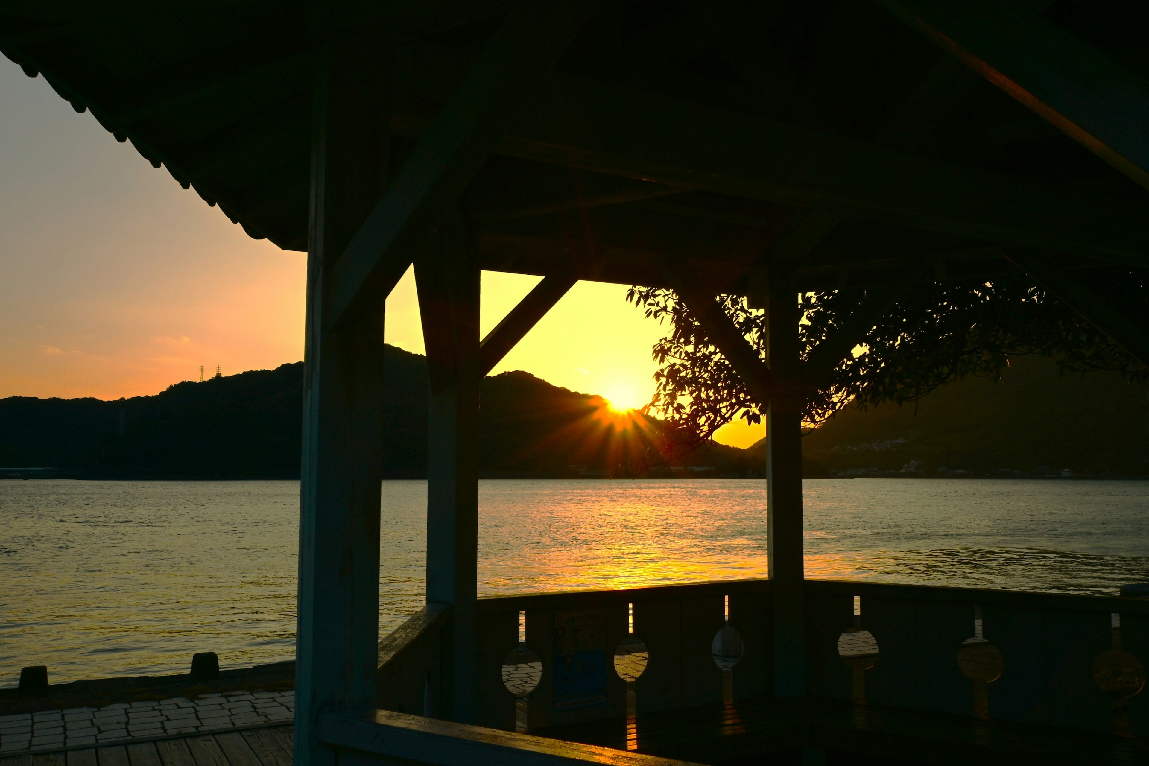 A beautiful sunset over a lake with a wooden pavilion in the foreground and silhouetted mountains in the background