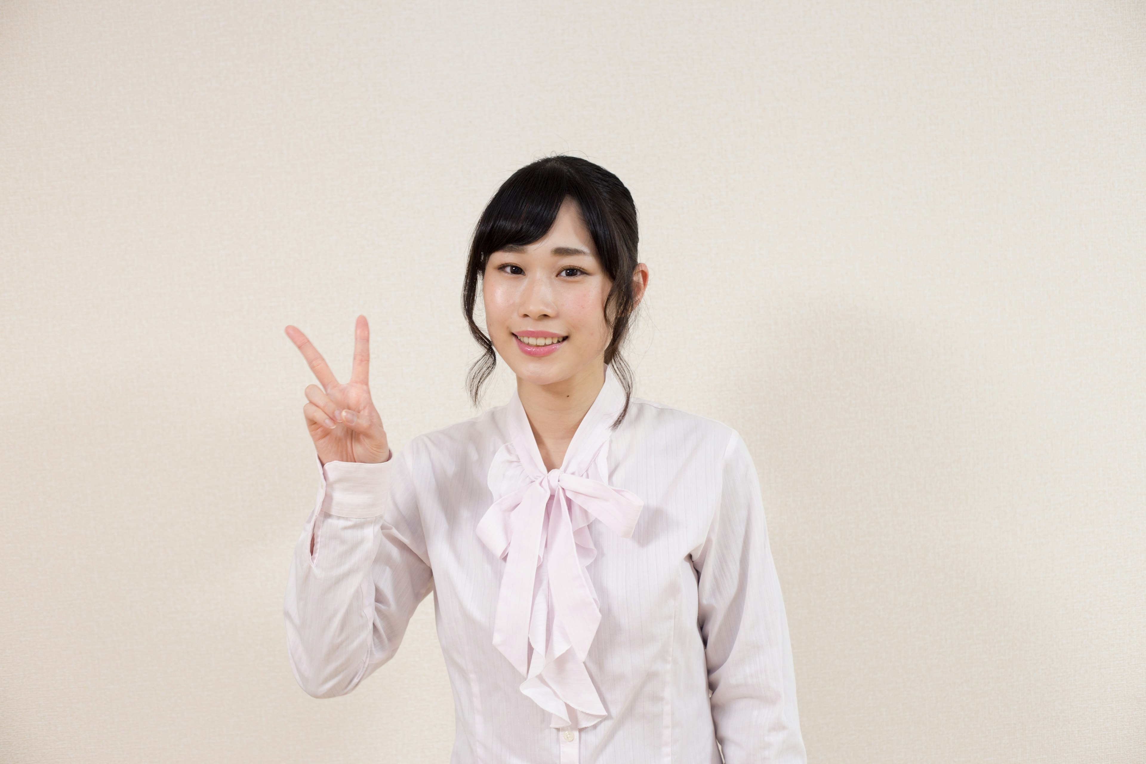 A woman in a white blouse making a peace sign with a smile