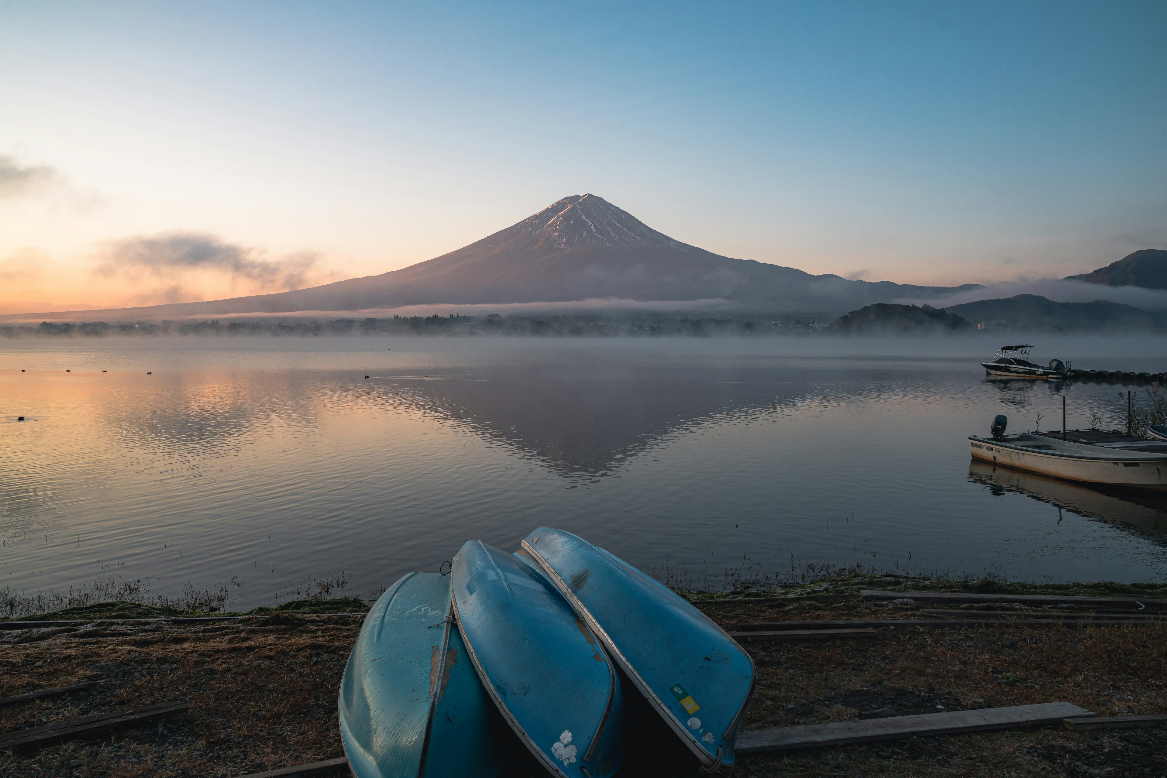 Monte Fuji riflesso su un lago calmo con barche blu in primo piano