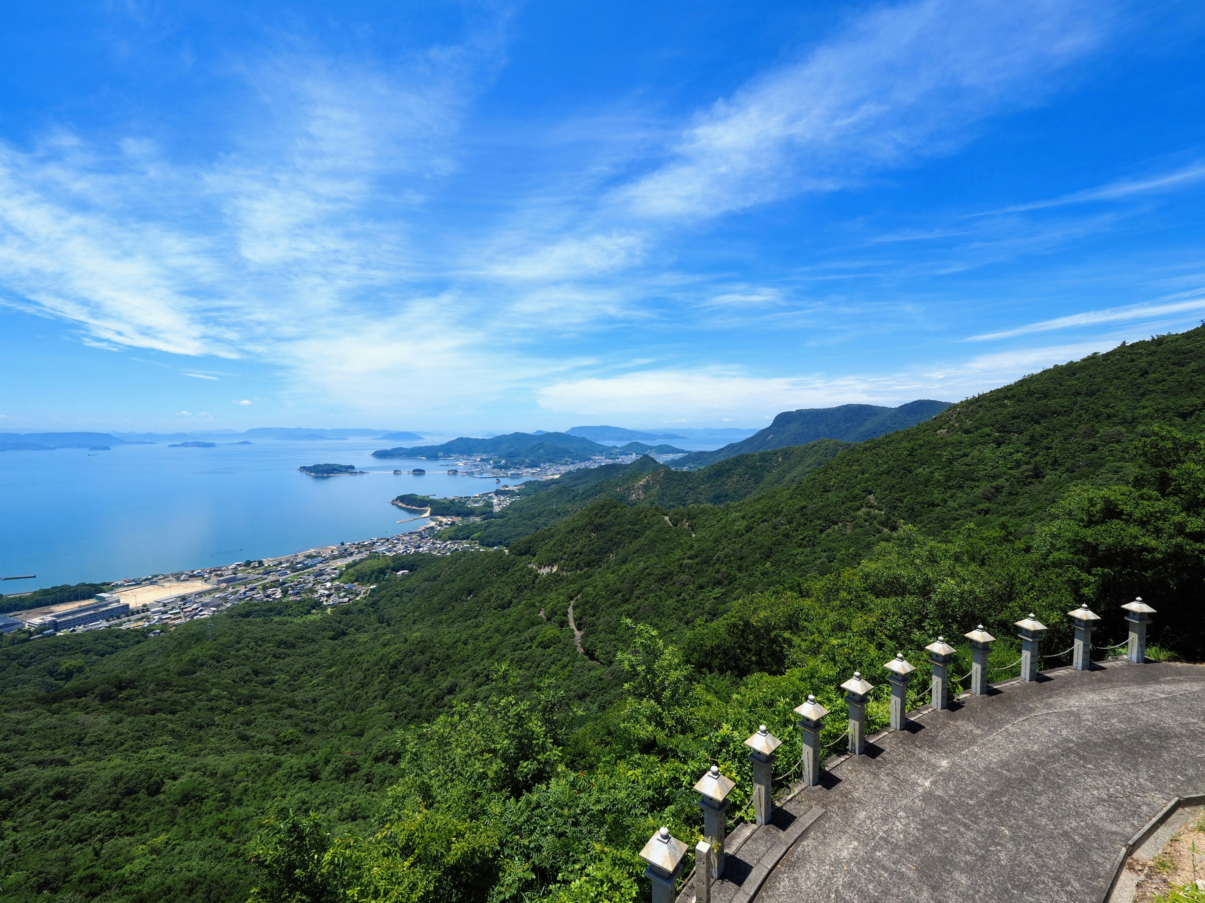 Scenic view of lush green mountains with blue sky and sea in the background featuring stone lanterns