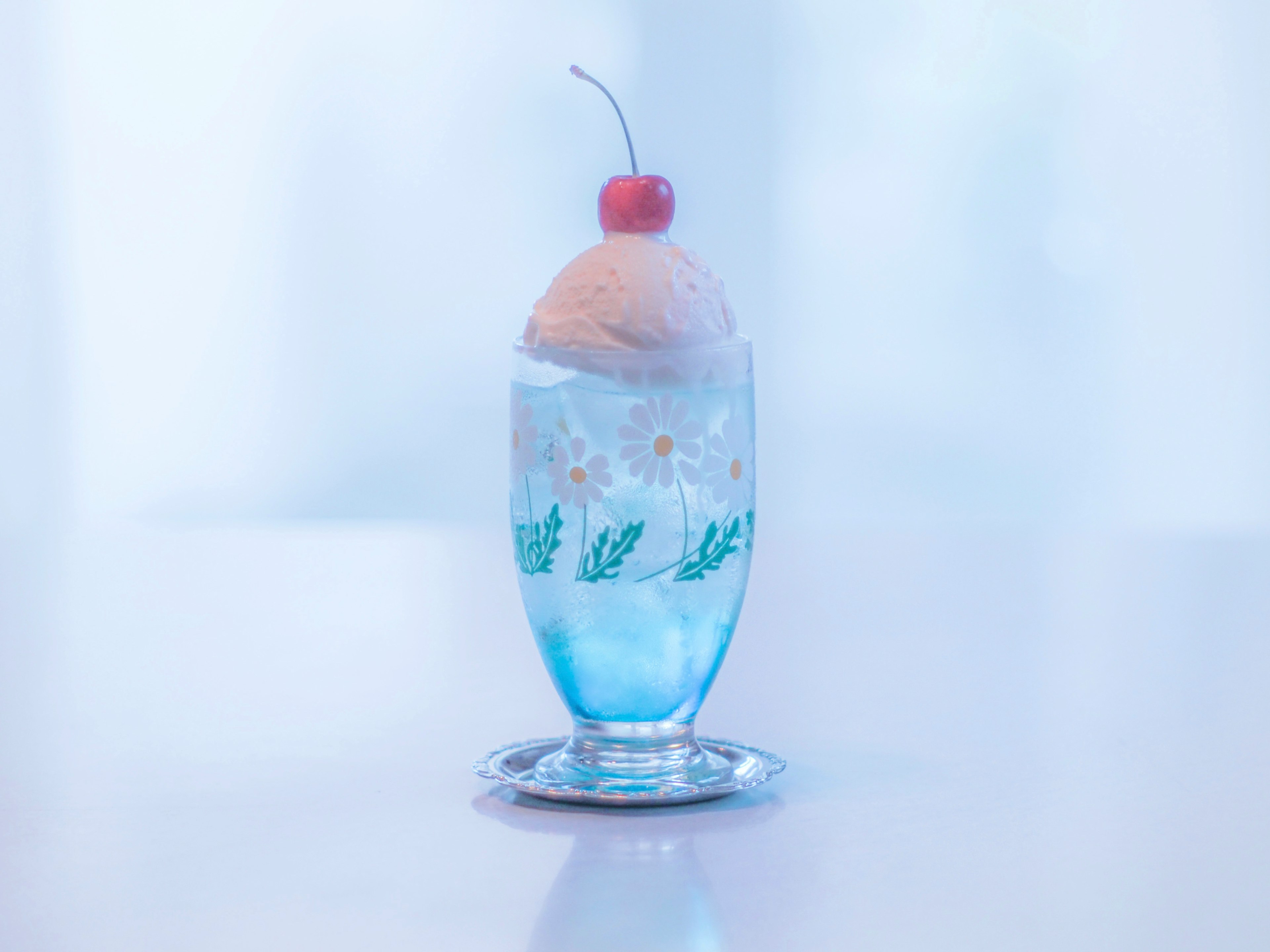 A dessert with ice cream in a blue glass topped with a red cherry