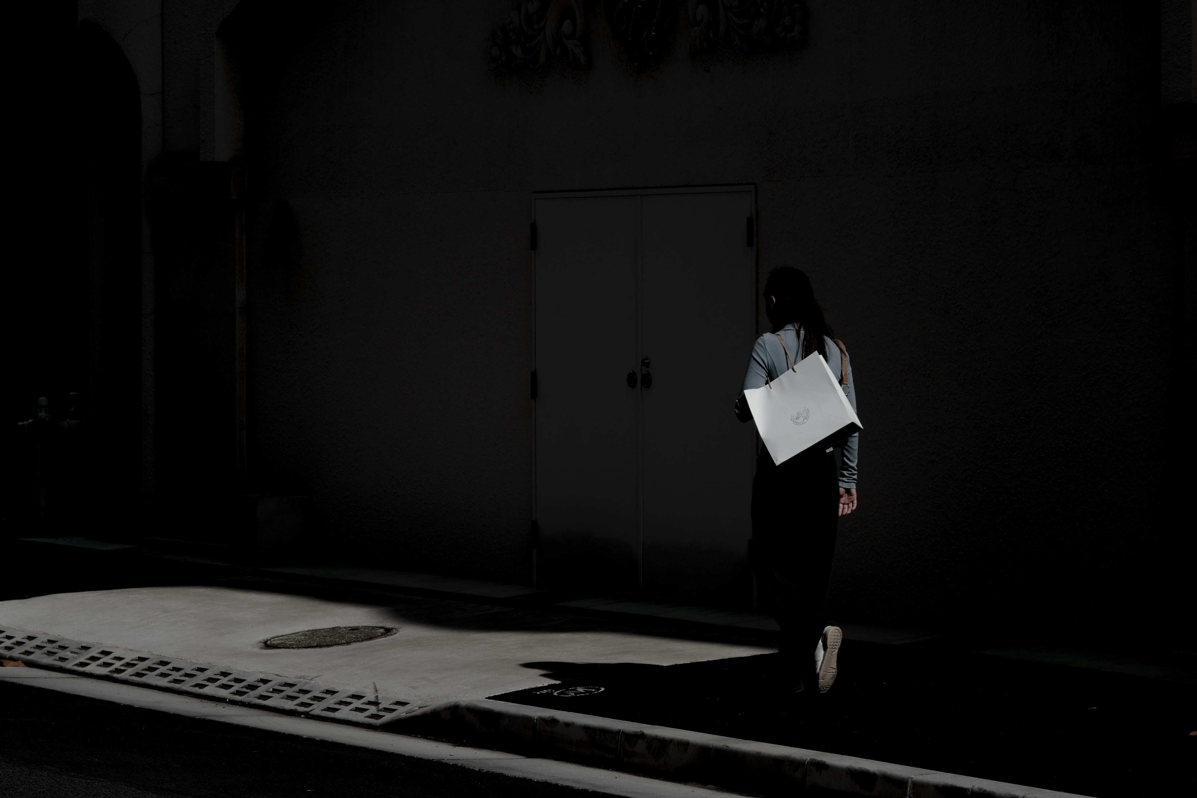 Femme marchant dans un cadre sombre tenant un sac blanc fort contraste entre lumière et ombre