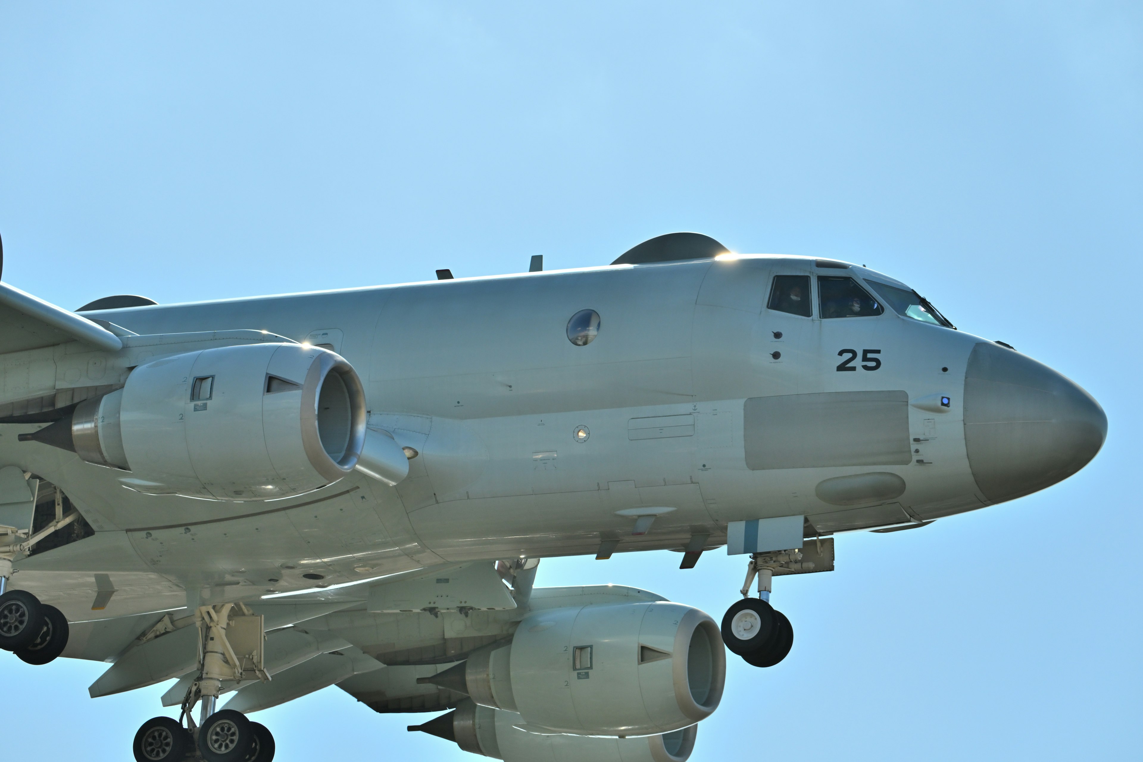 Avion argenté volant contre un ciel bleu montrant son corps supérieur et ses moteurs