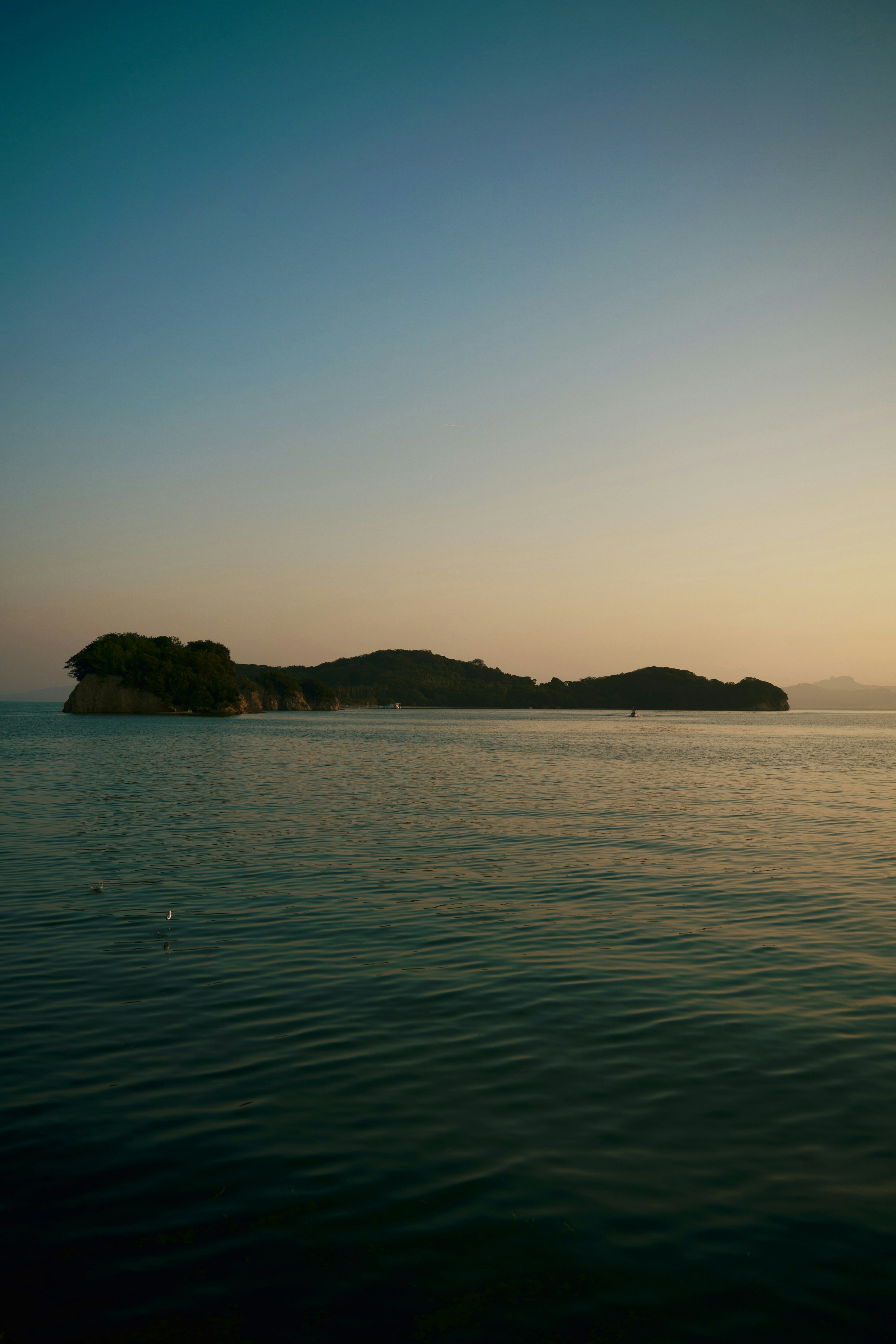 Pemandangan laut yang tenang dengan siluet pulau terpencil saat matahari terbenam yang indah