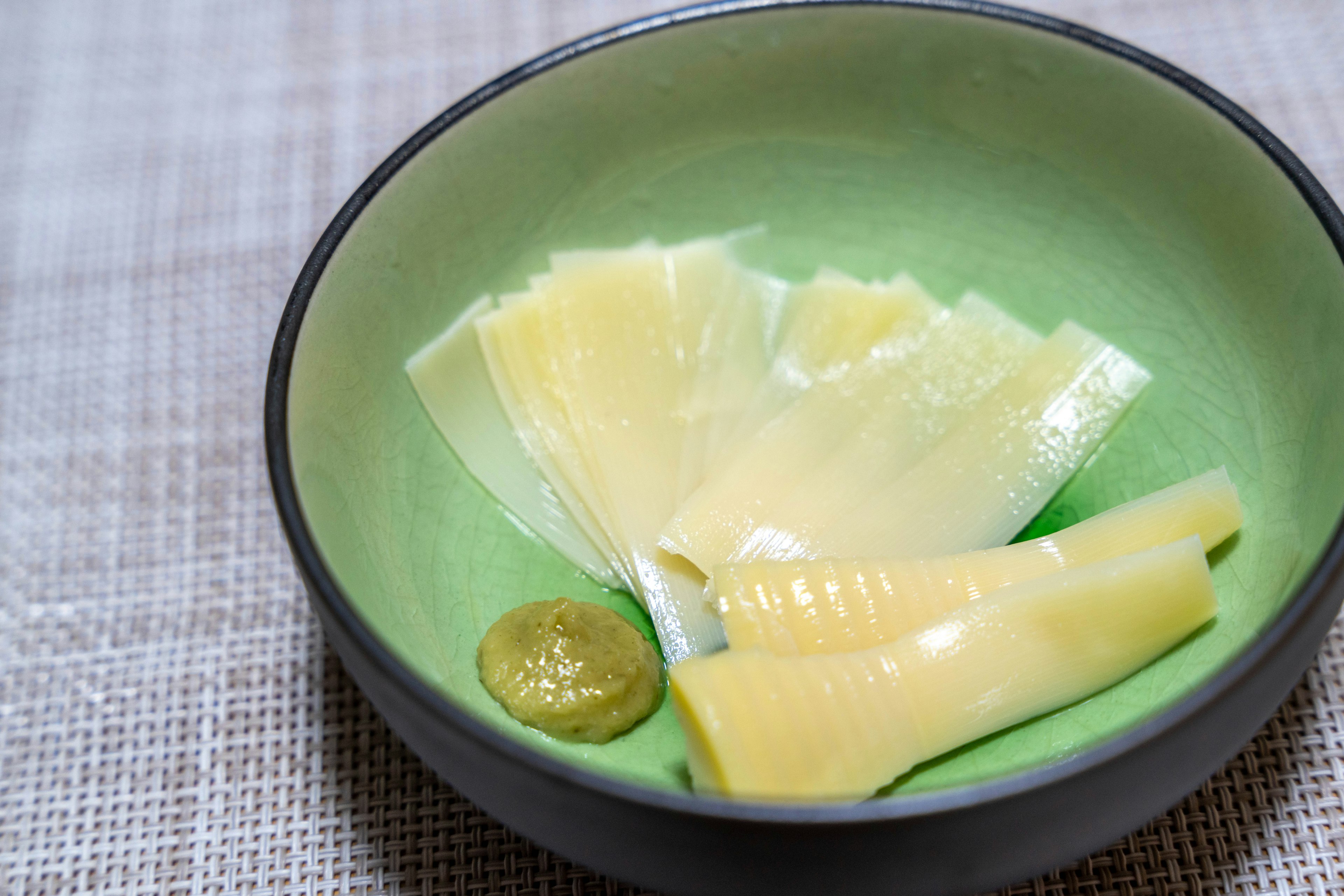 Thin slices of bamboo shoots served with wasabi in a green bowl