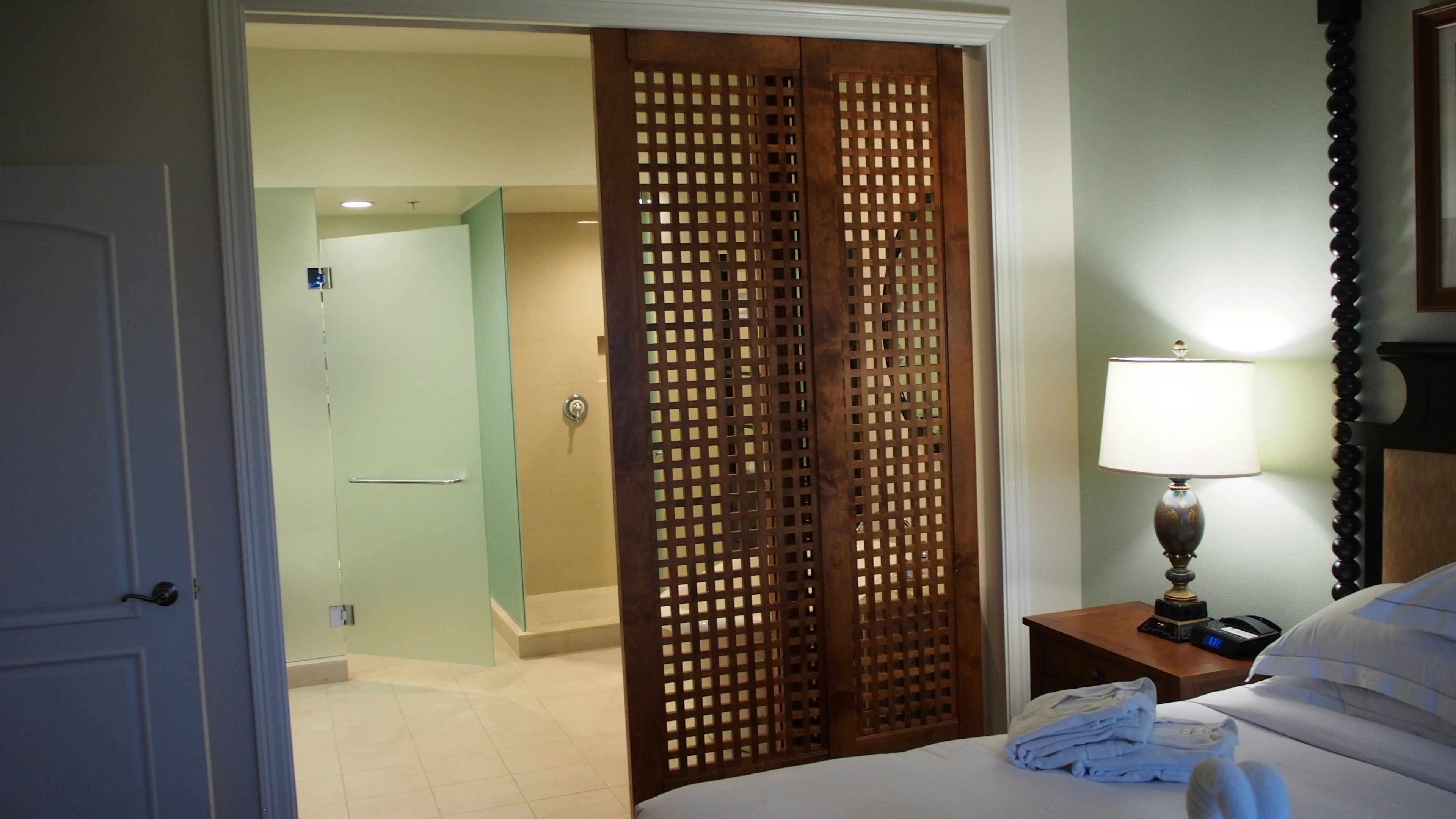 Vue d'une porte coulissante en bois menant à une salle de bain depuis une chambre avec une lampe