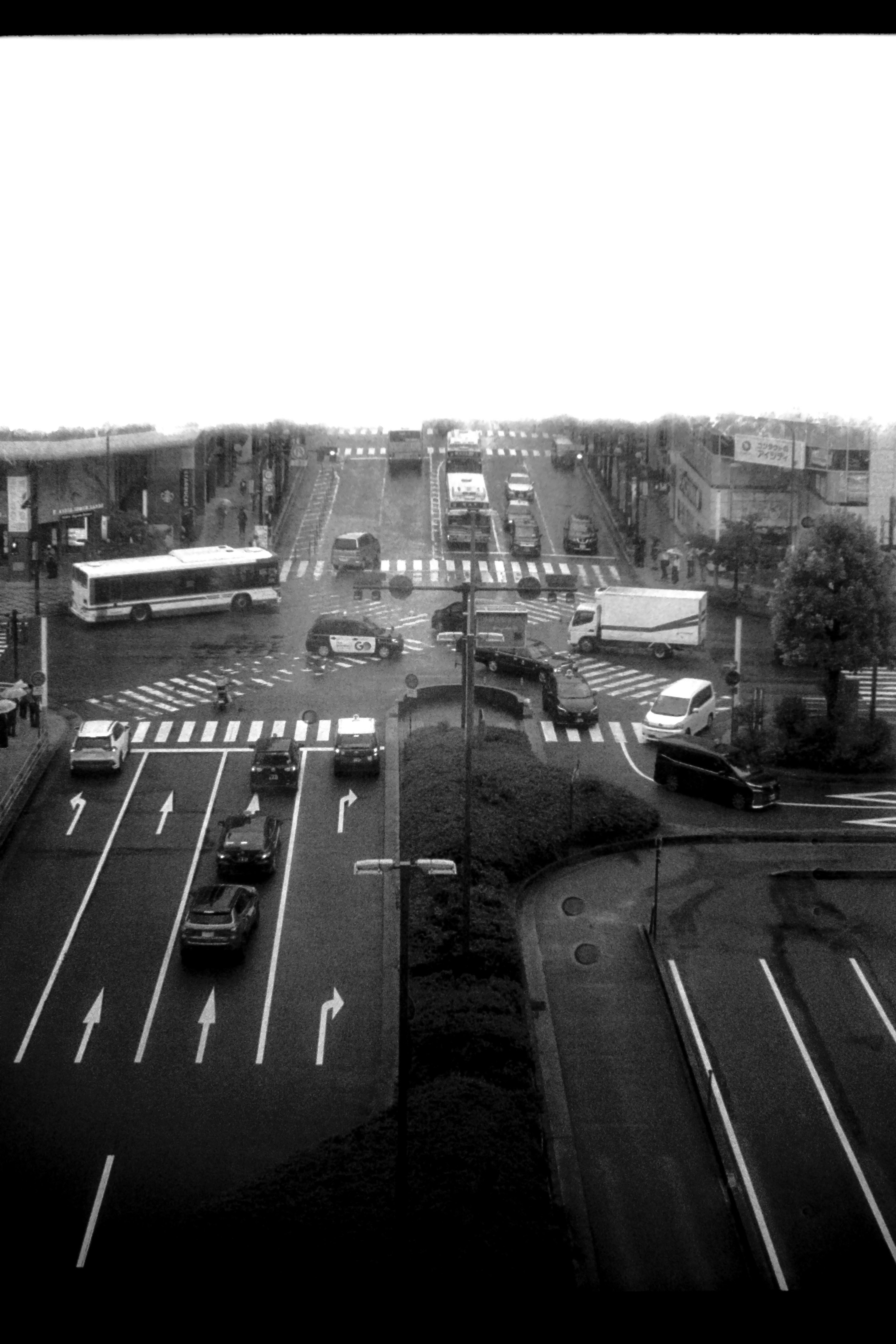 Monochrome image of an intersection showing traffic with vehicles and buses