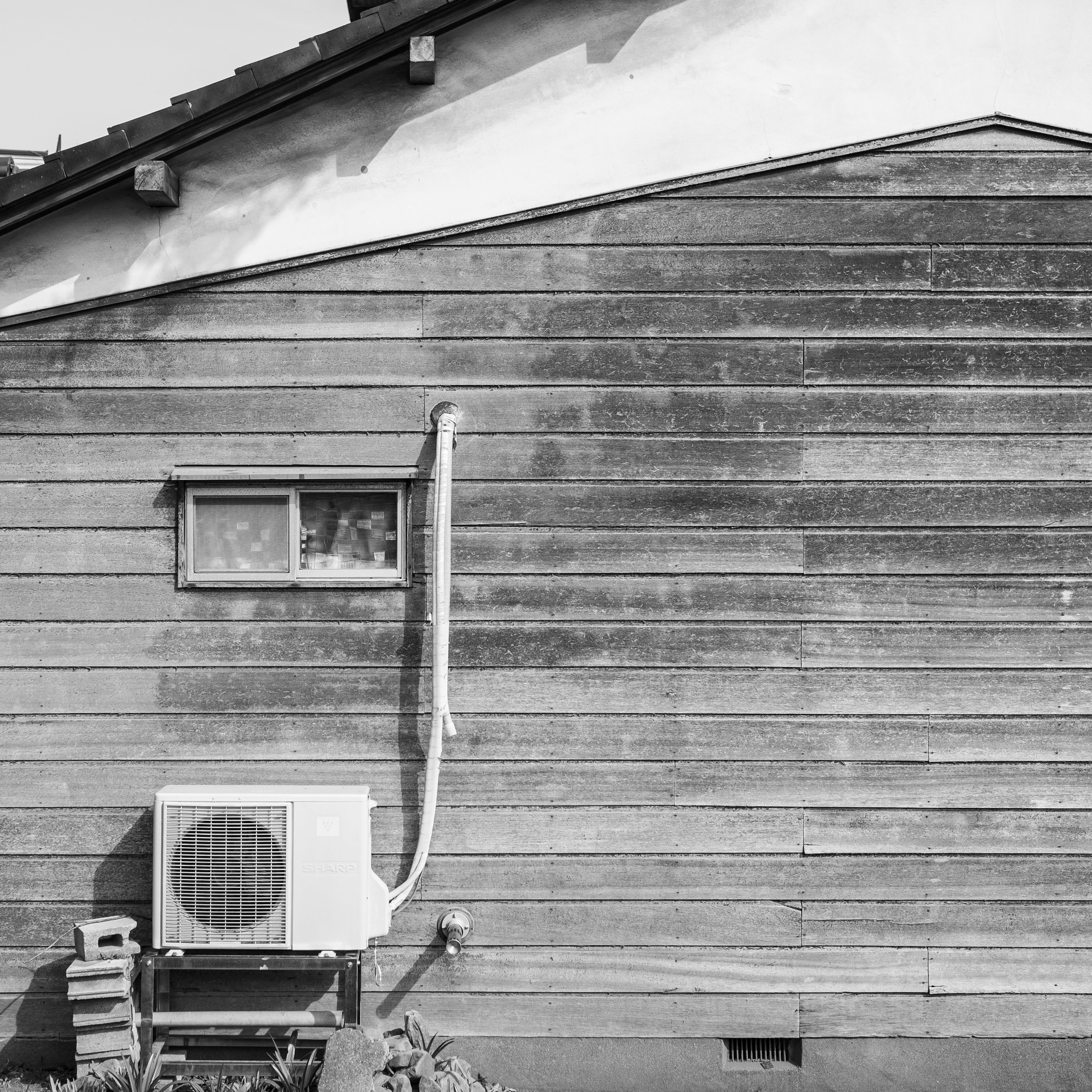 Wetterverbrannter Holzrahmen eines Hauses mit einer Klimaanlage und einem Fenster