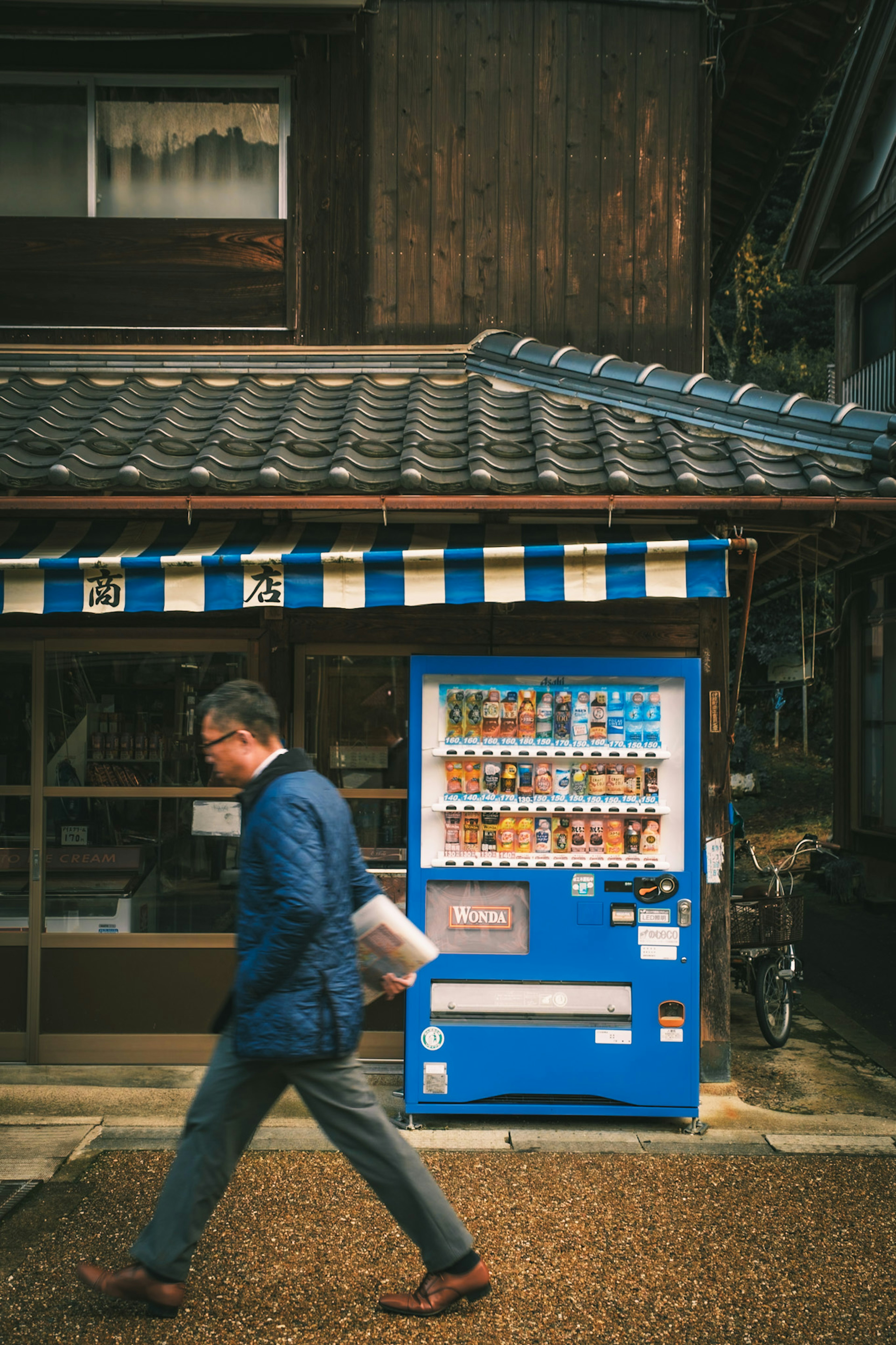 Ein Mann, der an einer blauen Verkaufsmaschine vor einem traditionellen japanischen Gebäude vorbeigeht