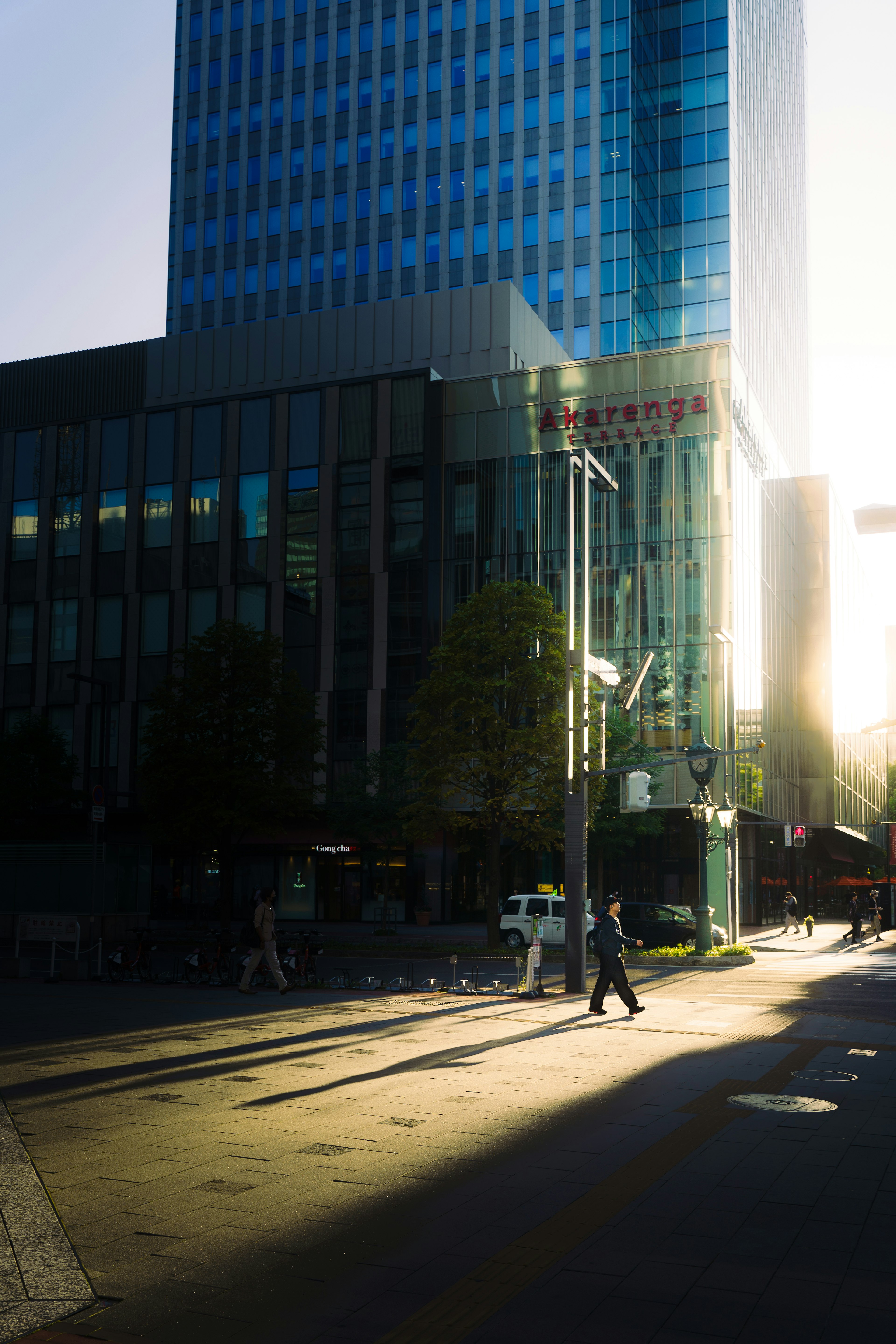 Edificio moderno reflejando la luz del atardecer con peatones en la calle