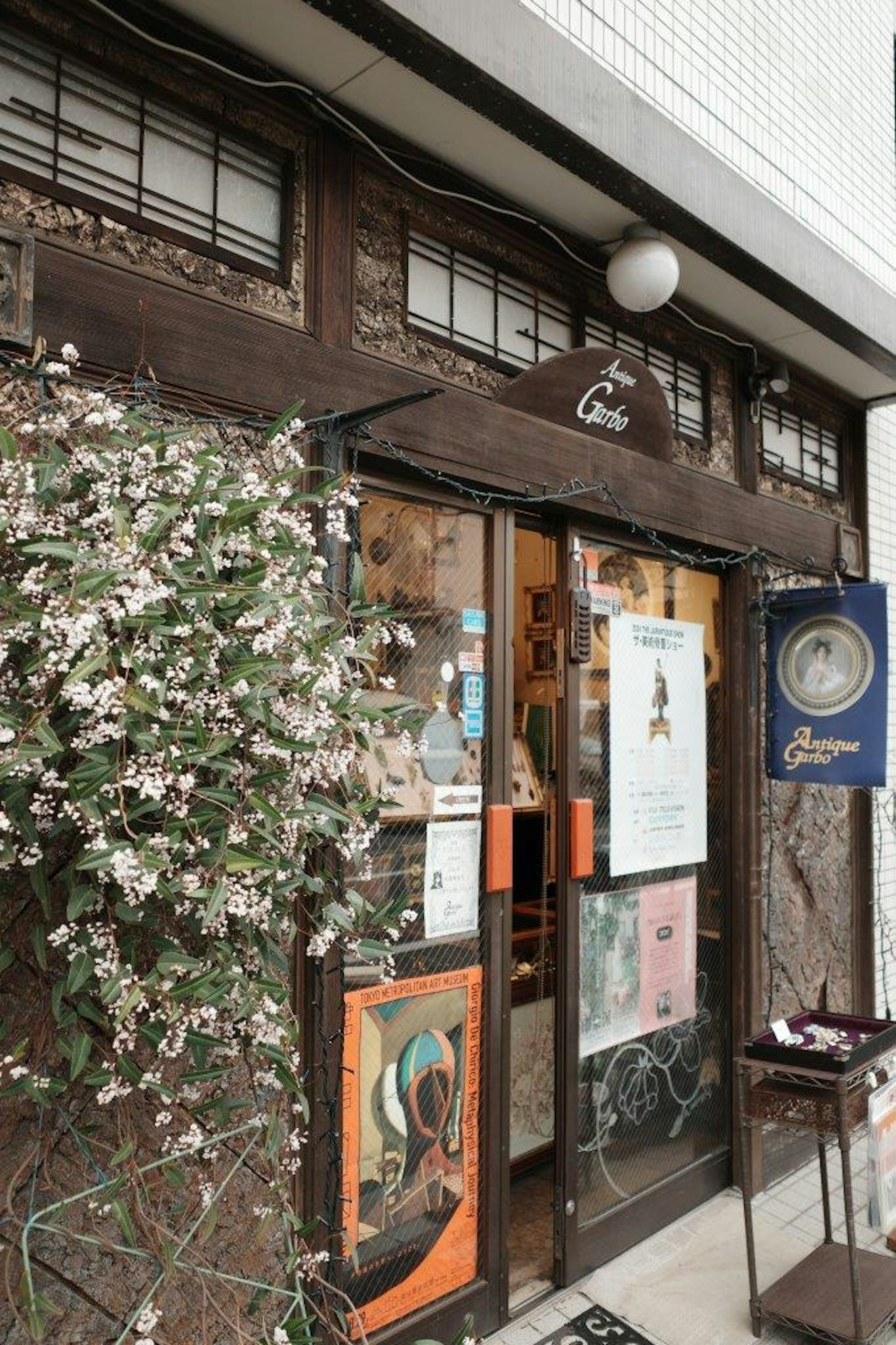 Ingresso di un antico caffè in legno con fiori bianchi e manifesti colorati