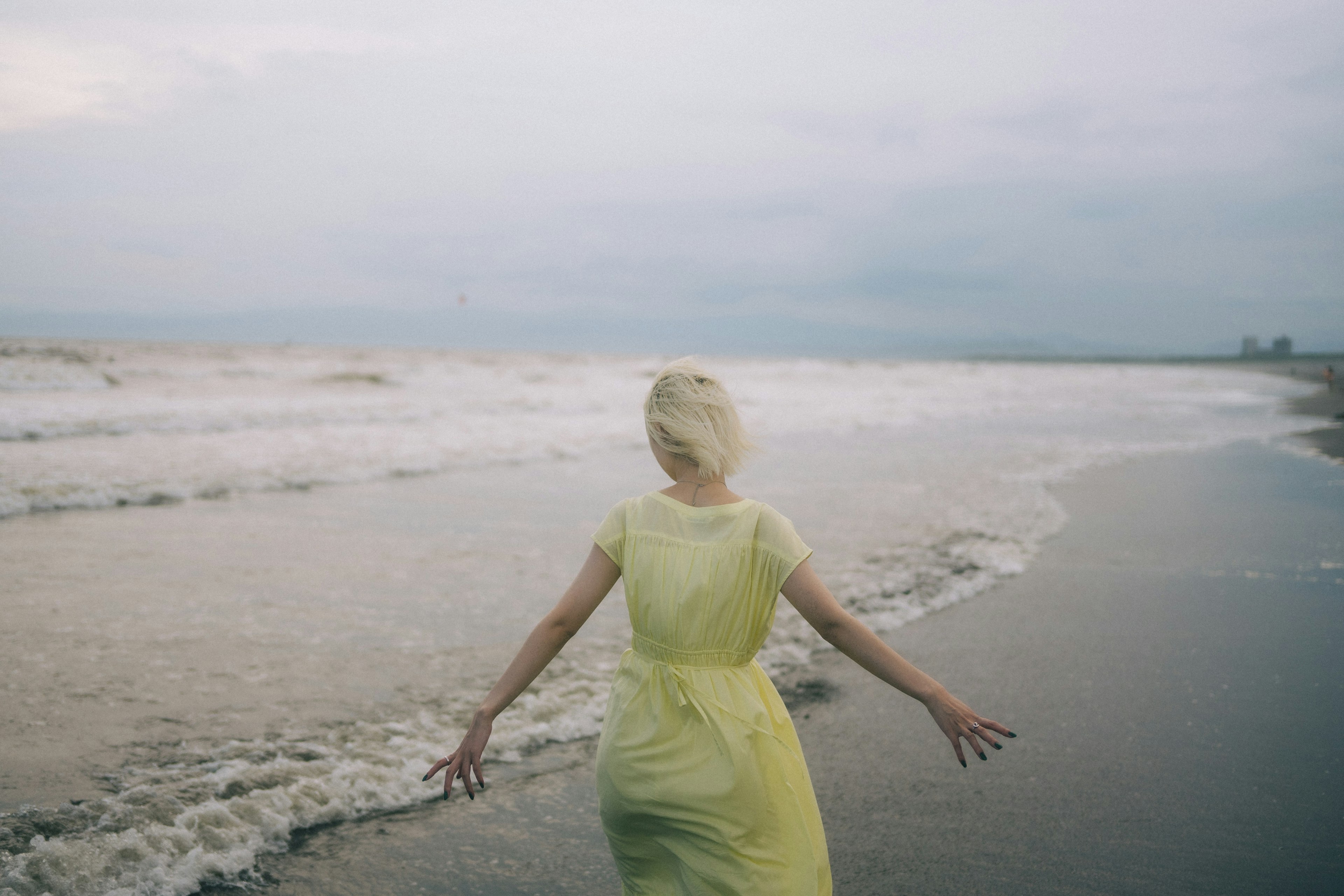 ผู้หญิงในชุดสีเหลืองยืนอยู่ที่ชายหาดหันหลังให้กล้อง