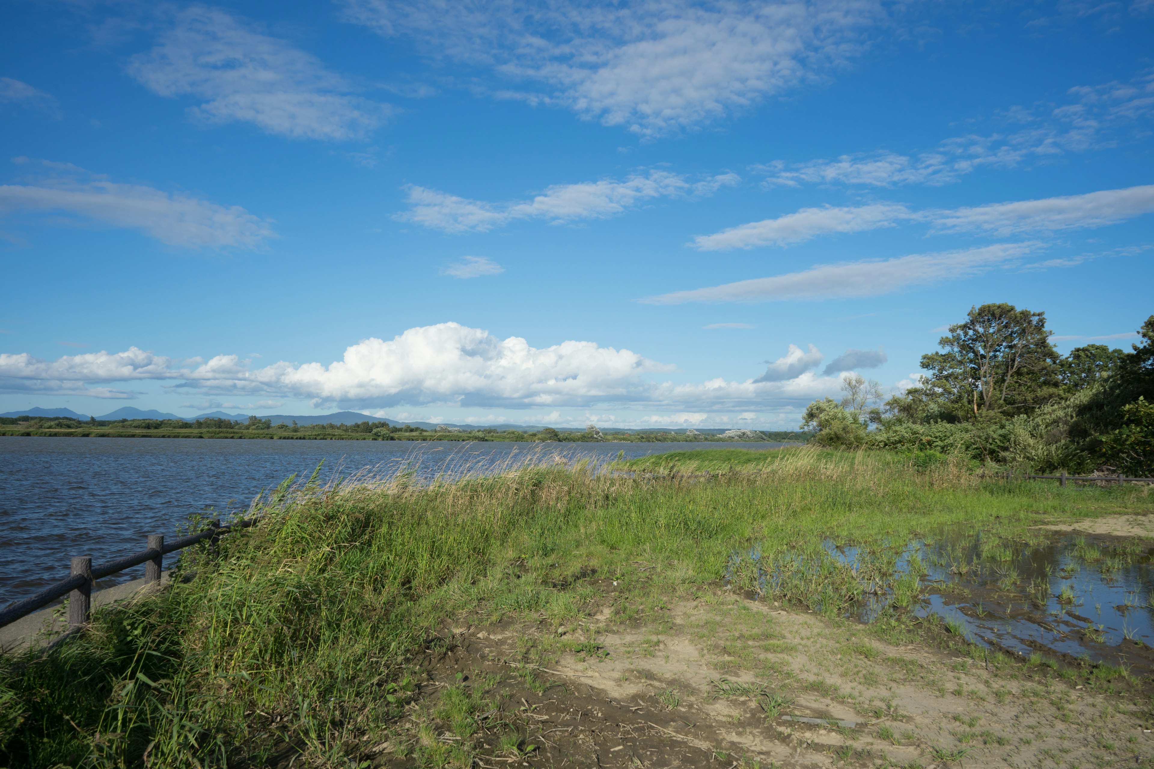 Landschaft mit blauem Himmel und weißen Wolken mit einem Fluss und einer grasbewachsenen Fläche