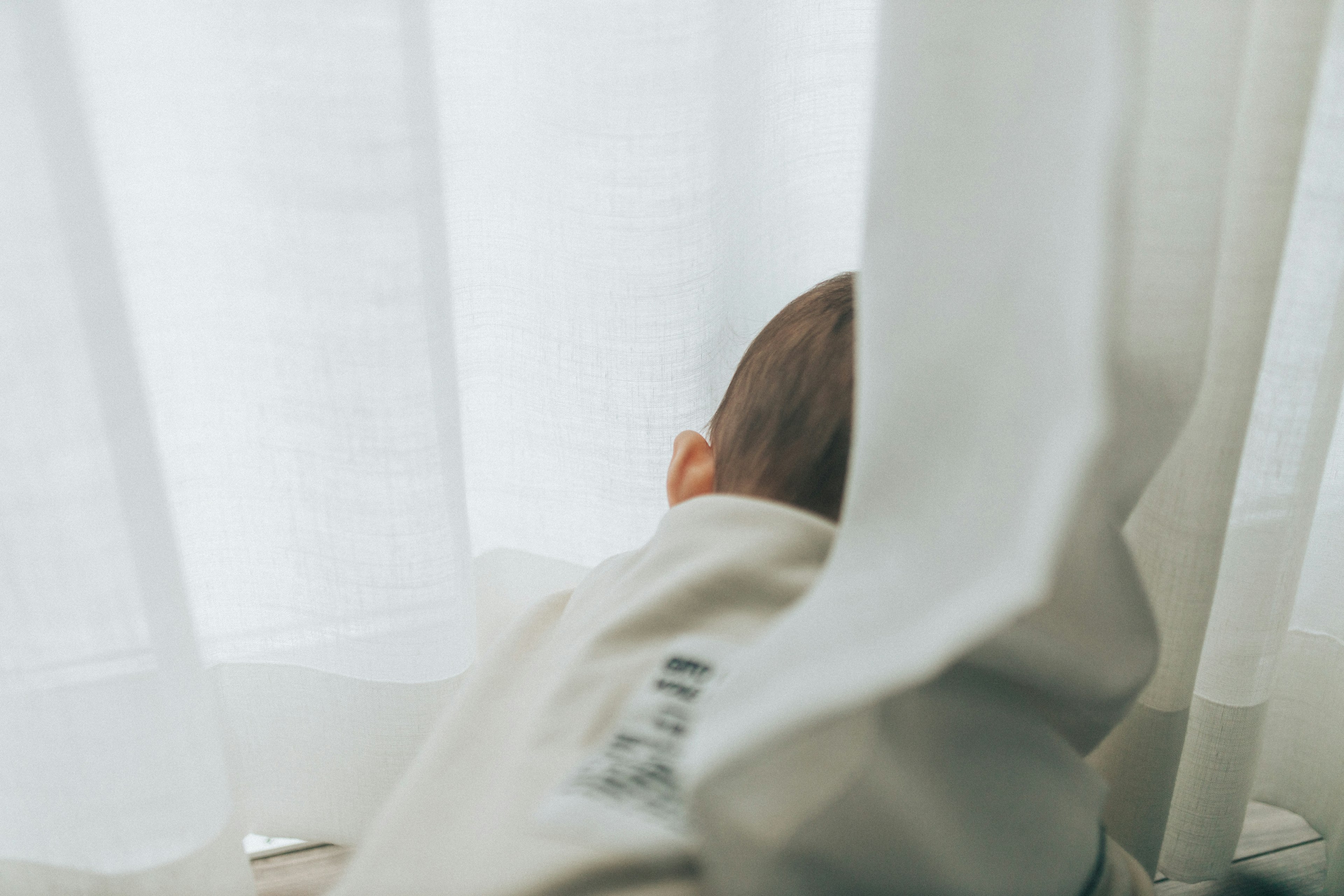 Enfant vu de dos derrière des rideaux blancs près d'une fenêtre