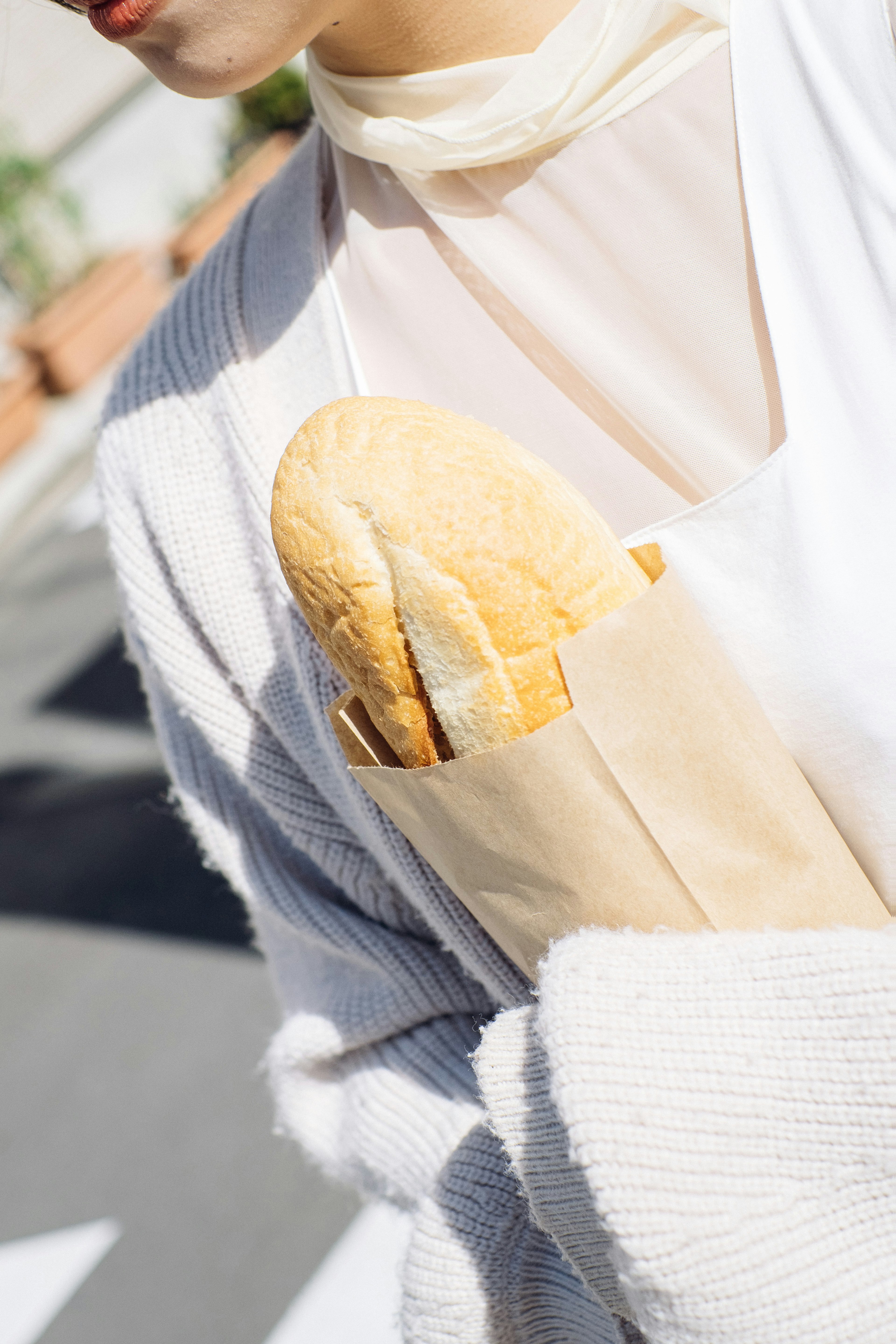 Woman in a white sweater holding a loaf of bread in a paper bag