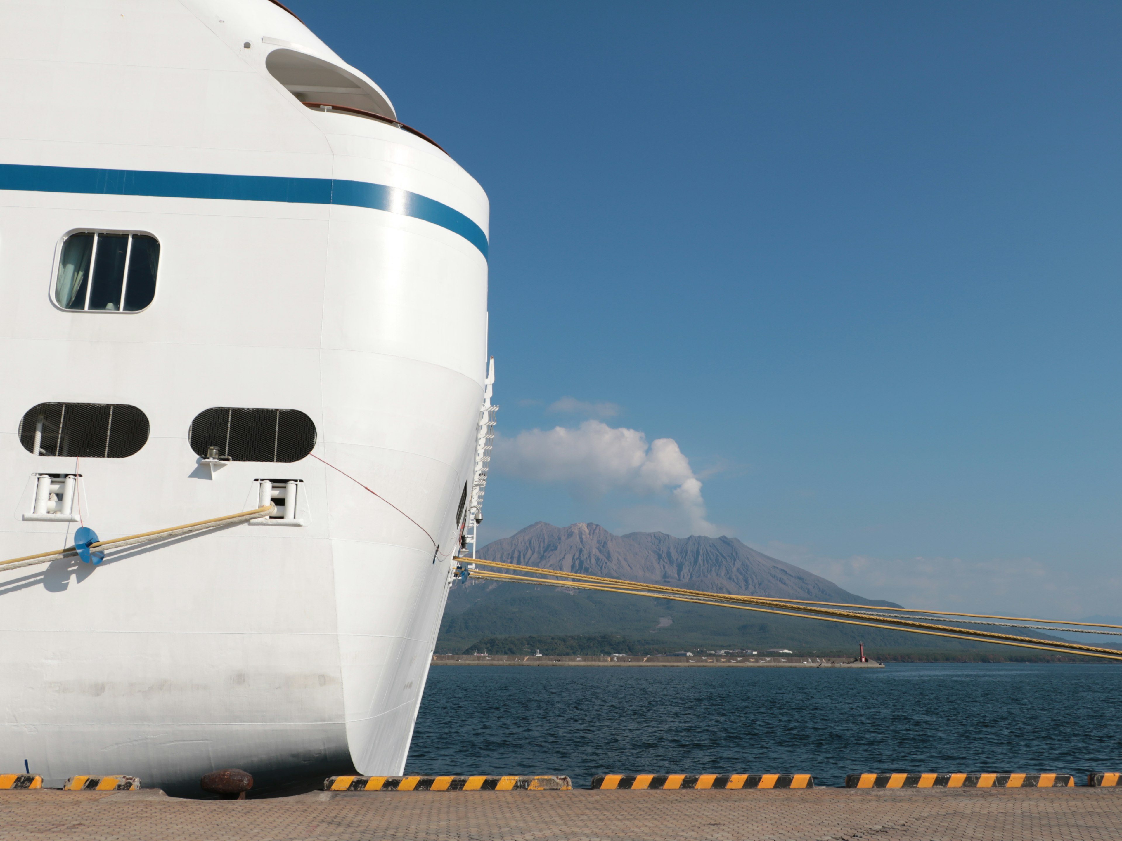 Bow of a white ship with blue accents against a clear sky and mountain backdrop