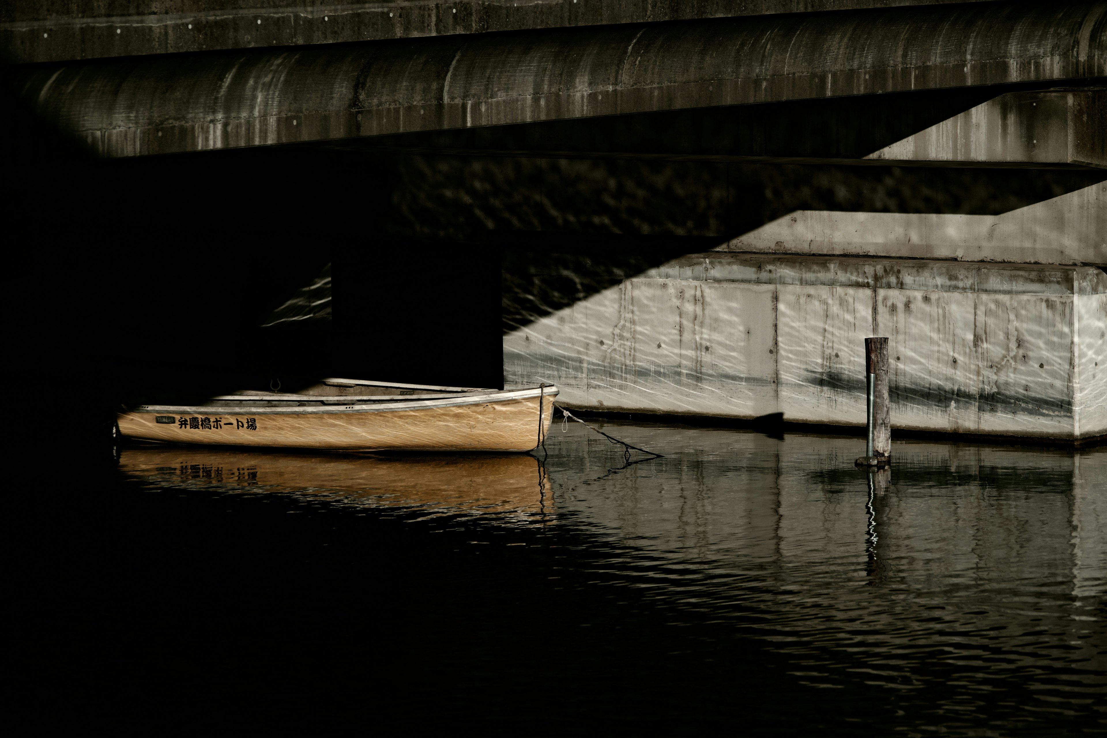 Ein gelbes Boot, das auf einer ruhigen Wasseroberfläche schwimmt, mit Schatten von einer Brücke