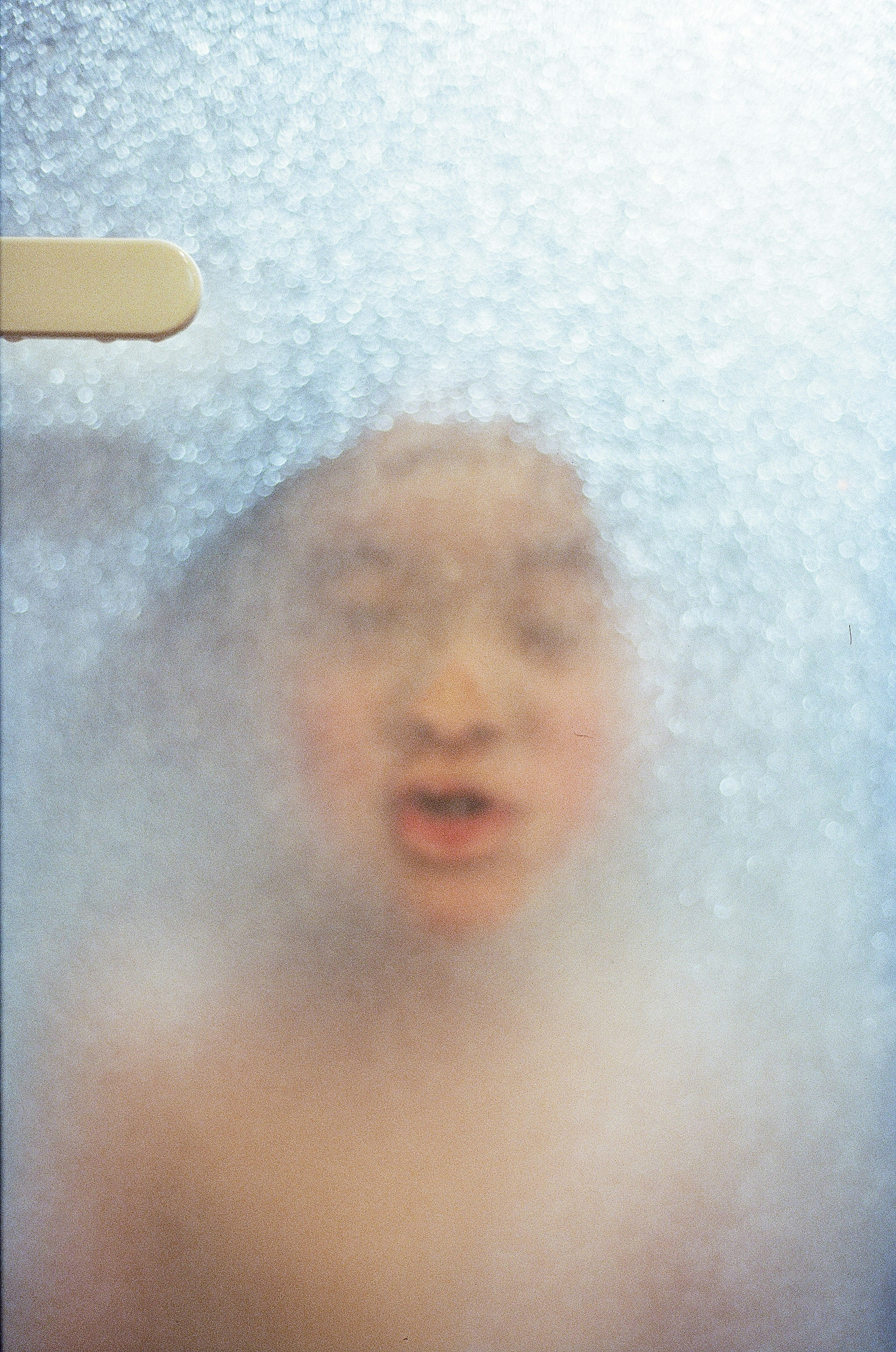 Child's face seen through foggy glass with steam creating a blurred effect