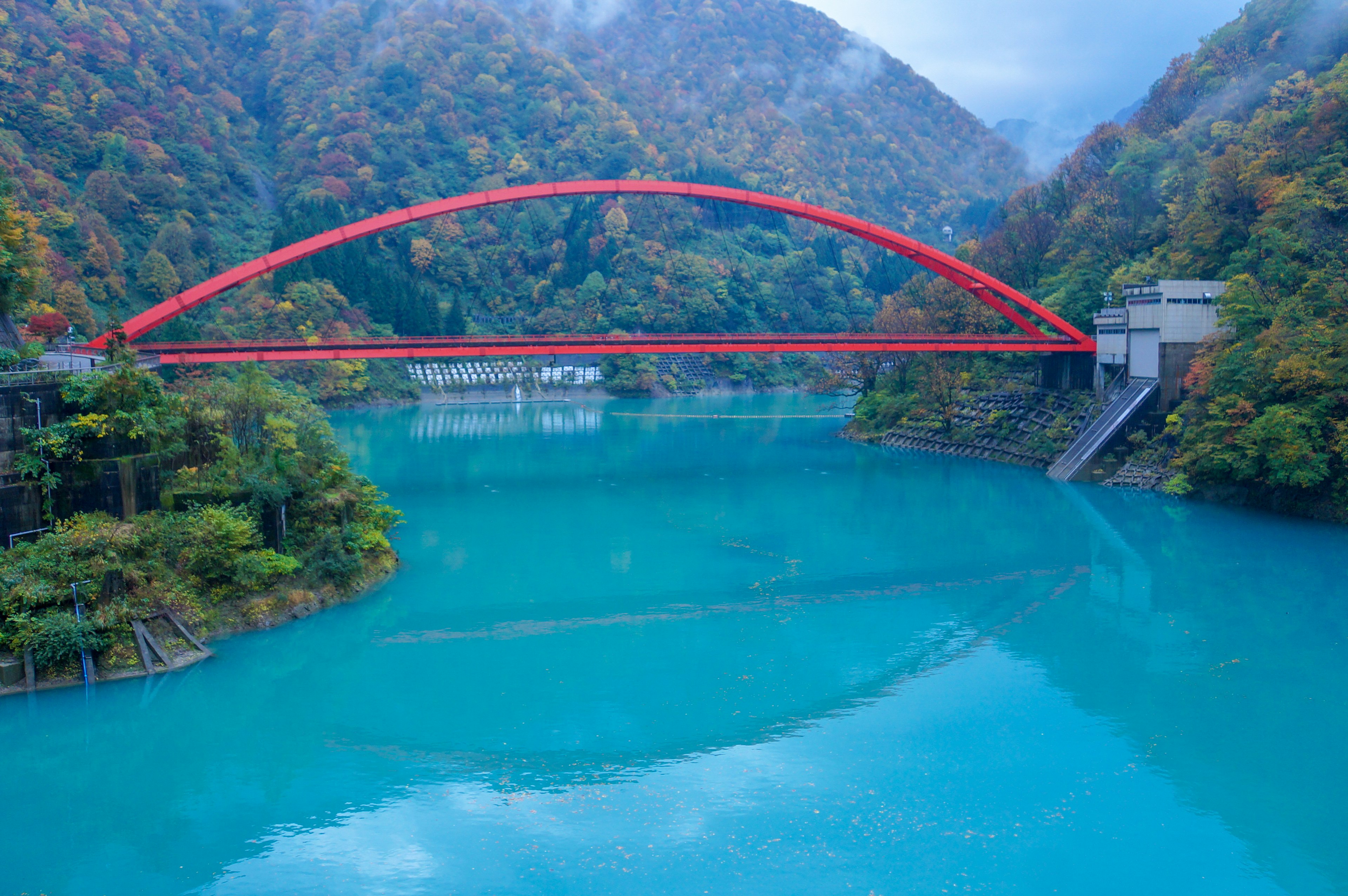 青い湖の上に架かる赤いアーチ橋と周囲の山々の秋の色