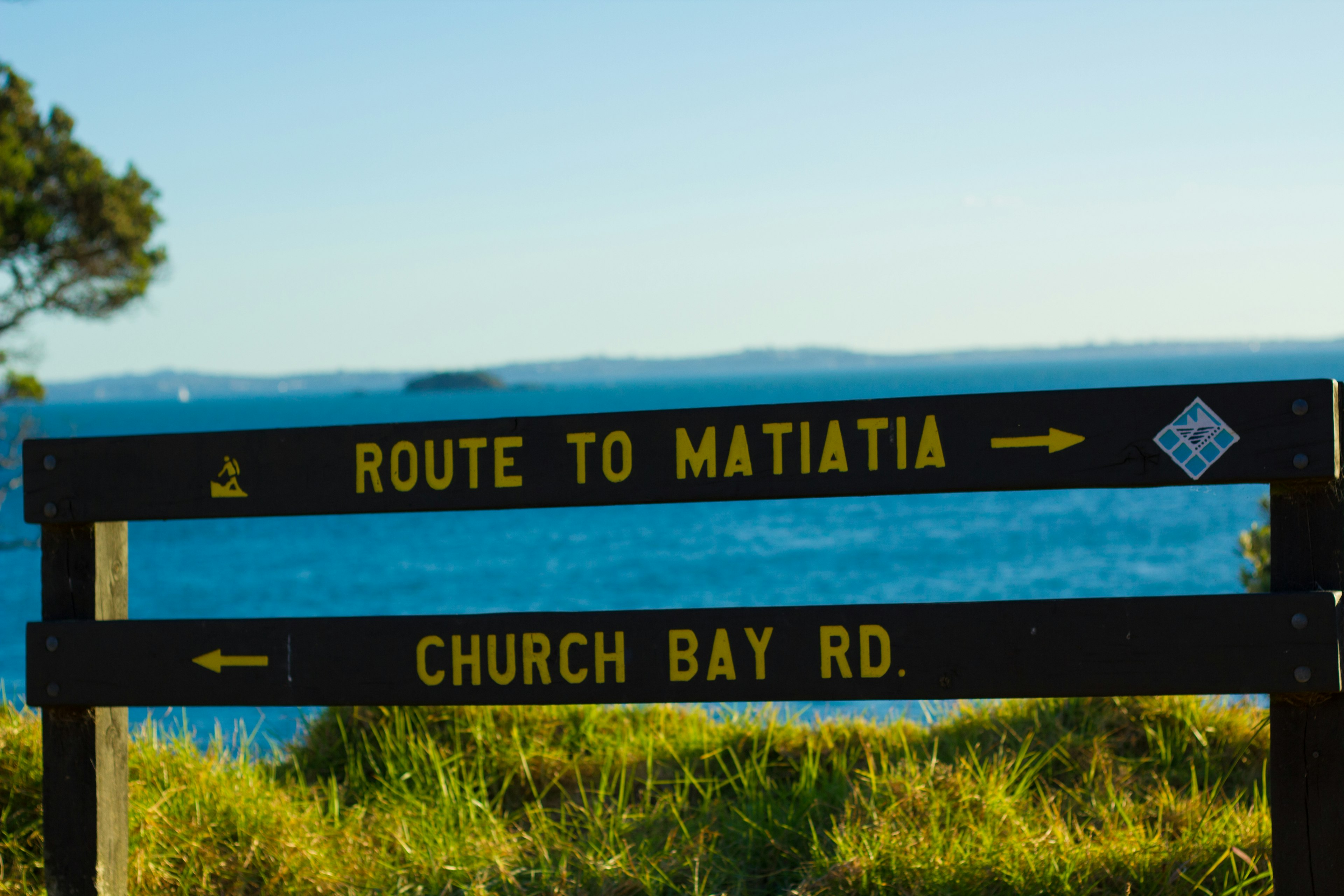 ป้ายบอกทางไป Matiatia และ Church Bay Road กับพื้นหลังทะเลสีน้ำเงิน