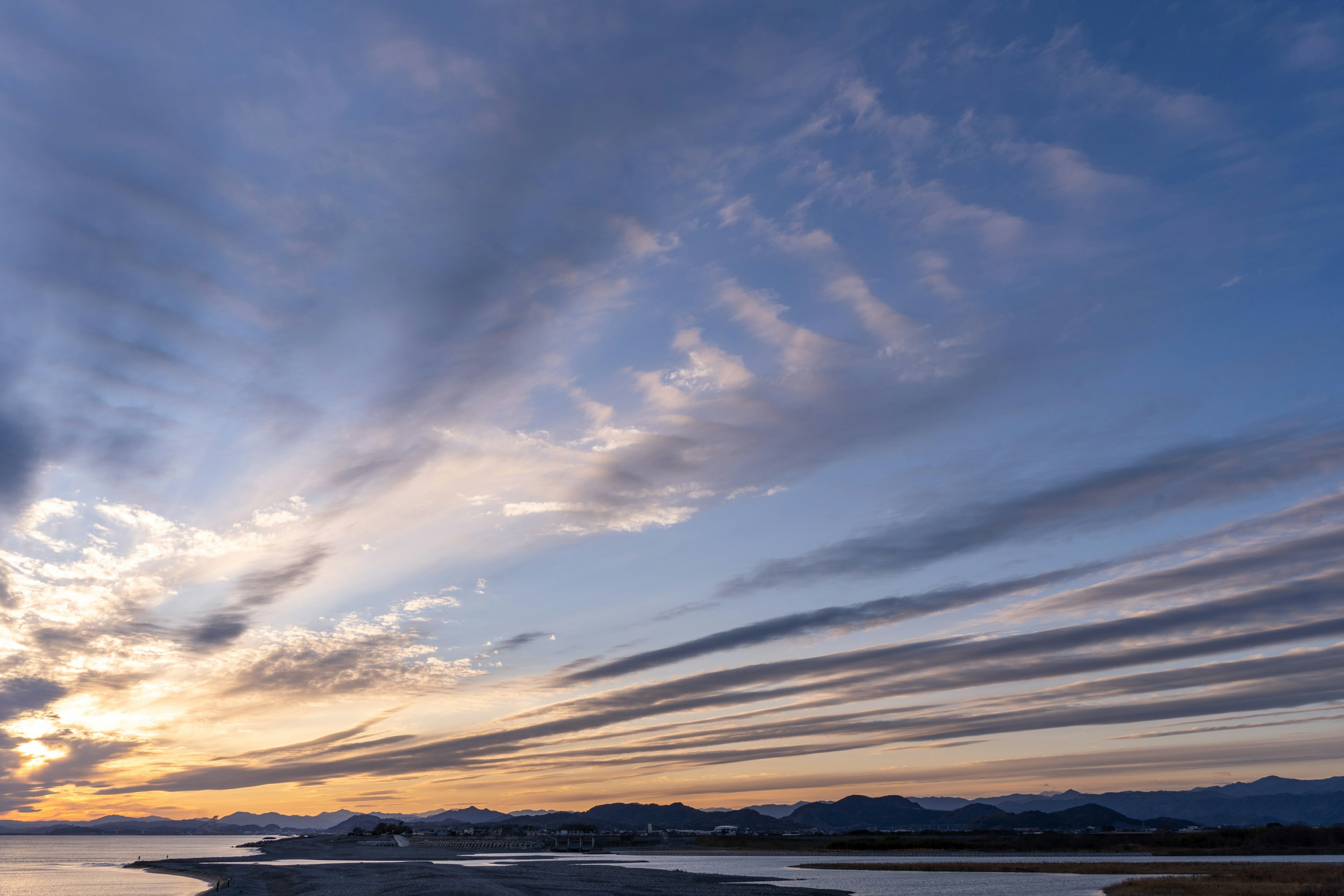 Schöner Sonnenuntergangshimmel mit gestreiften Wolken und Bergen