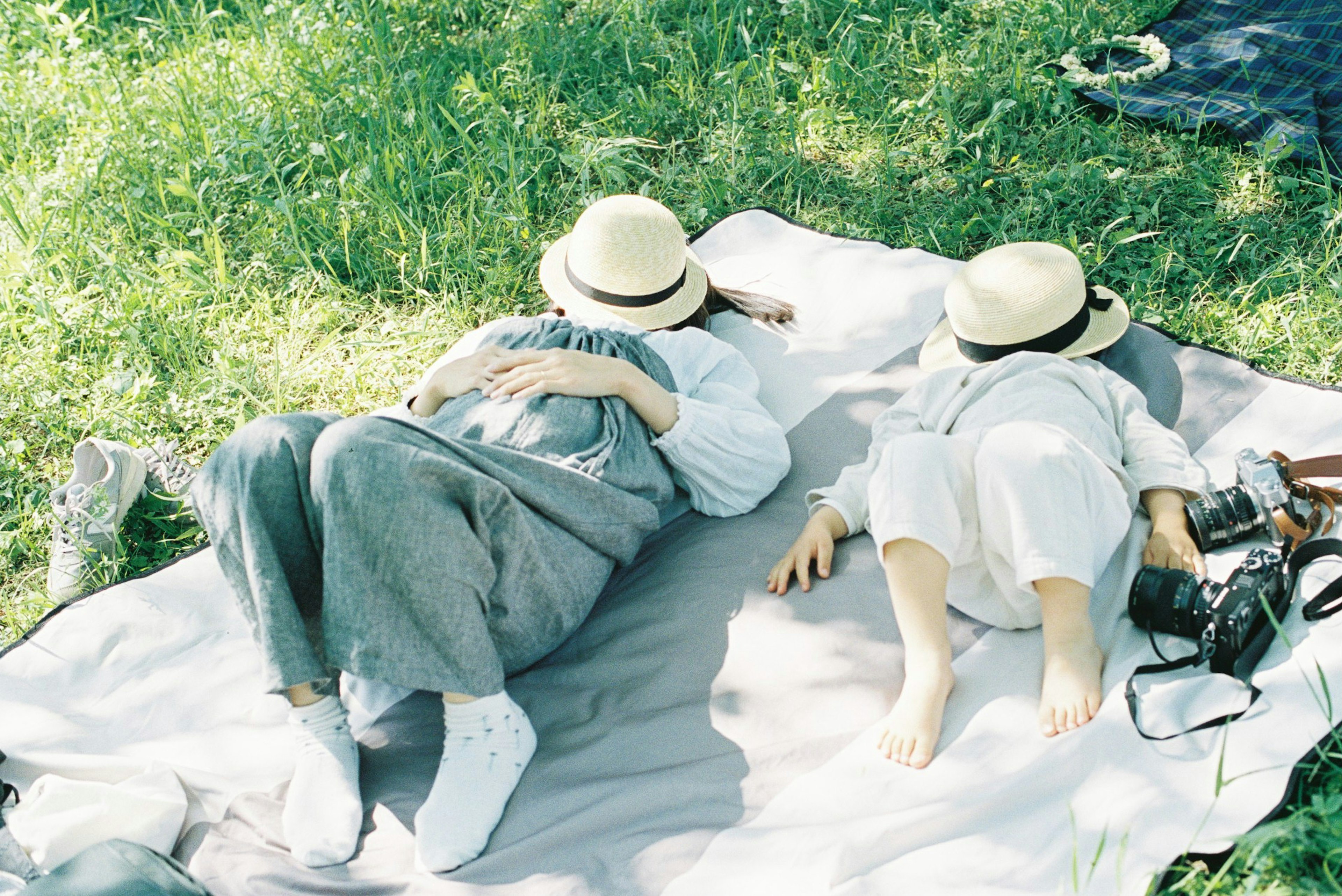 Dos personas acostadas sobre una manta de picnic en la hierba verde usando sombreros blancos