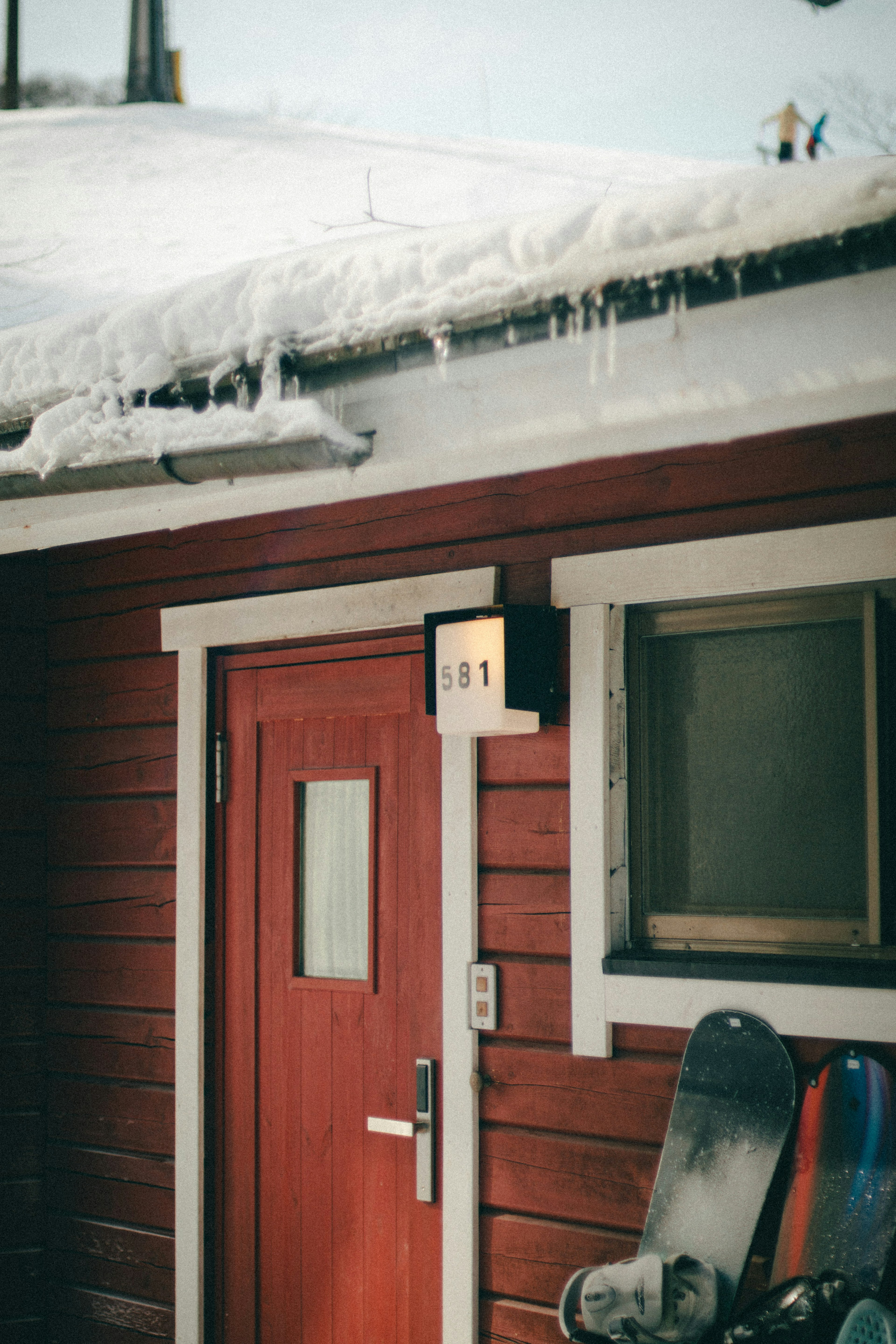 Red house door and window on a snowy day Snow-covered roof and snowboard