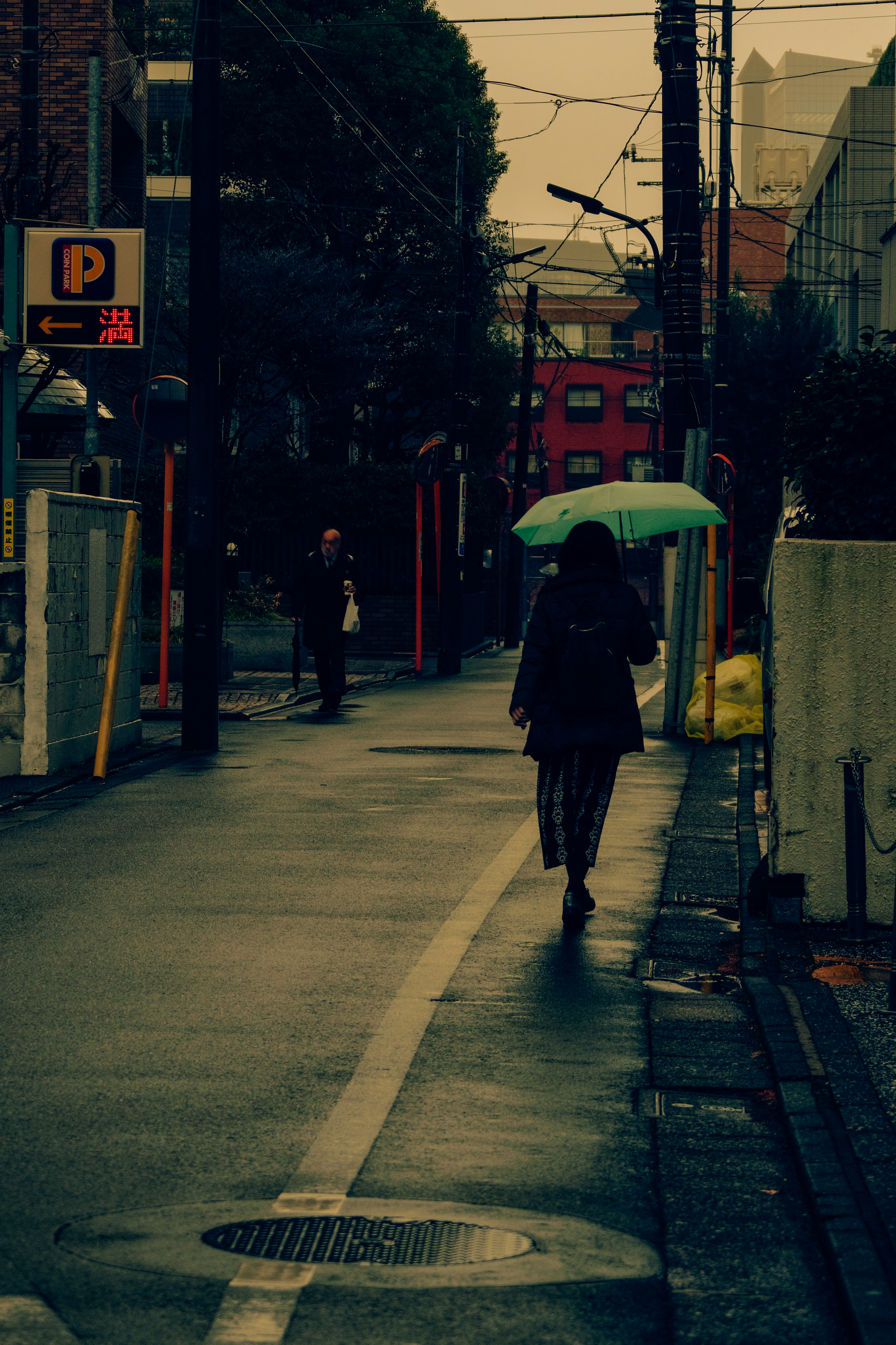 Eine Person, die mit einem grünen Regenschirm eine enge Straße im Regen entlanggeht