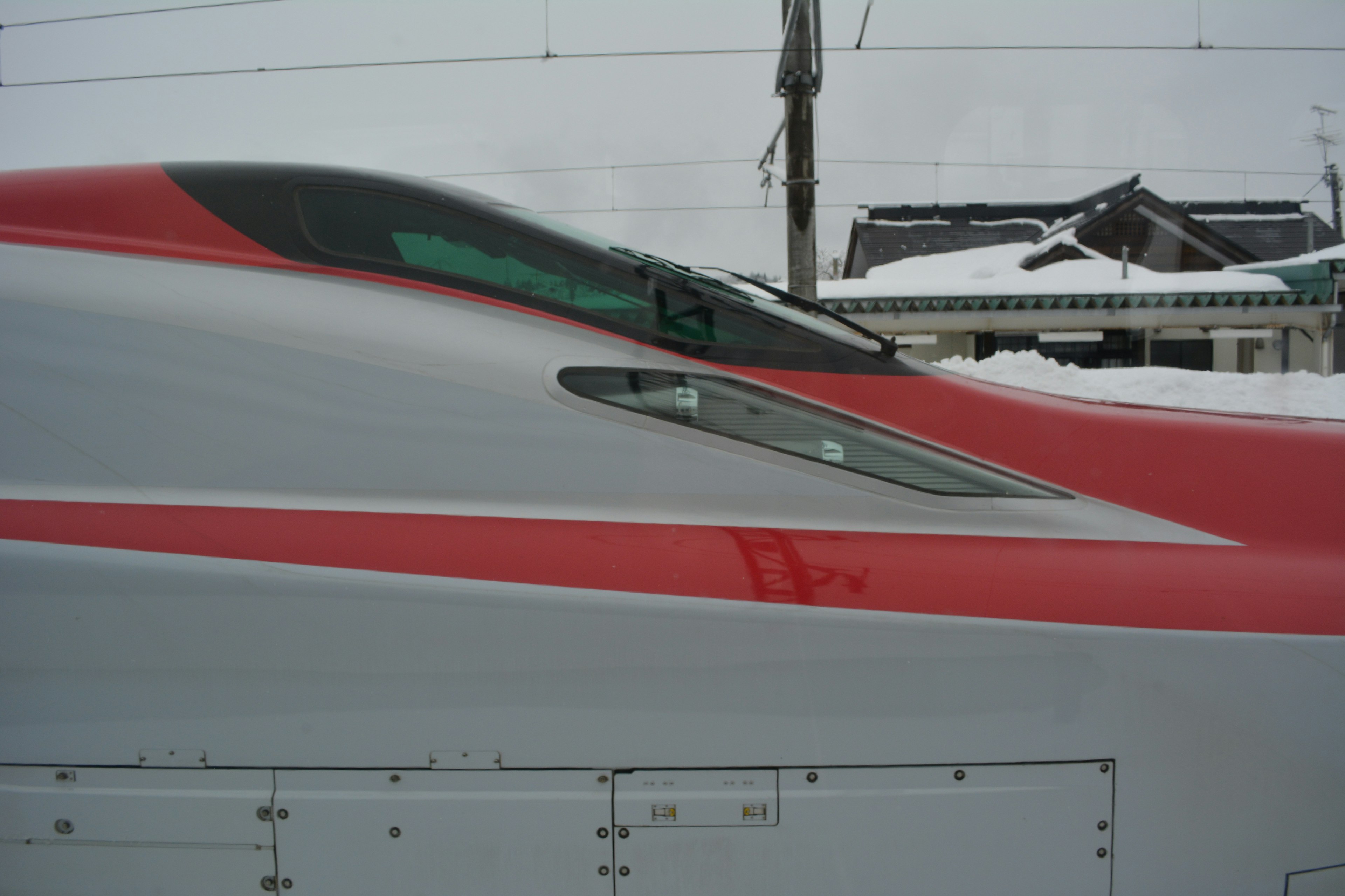 Close-up bagian depan kereta Shinkansen dengan desain aerodinamis dan aksen merah