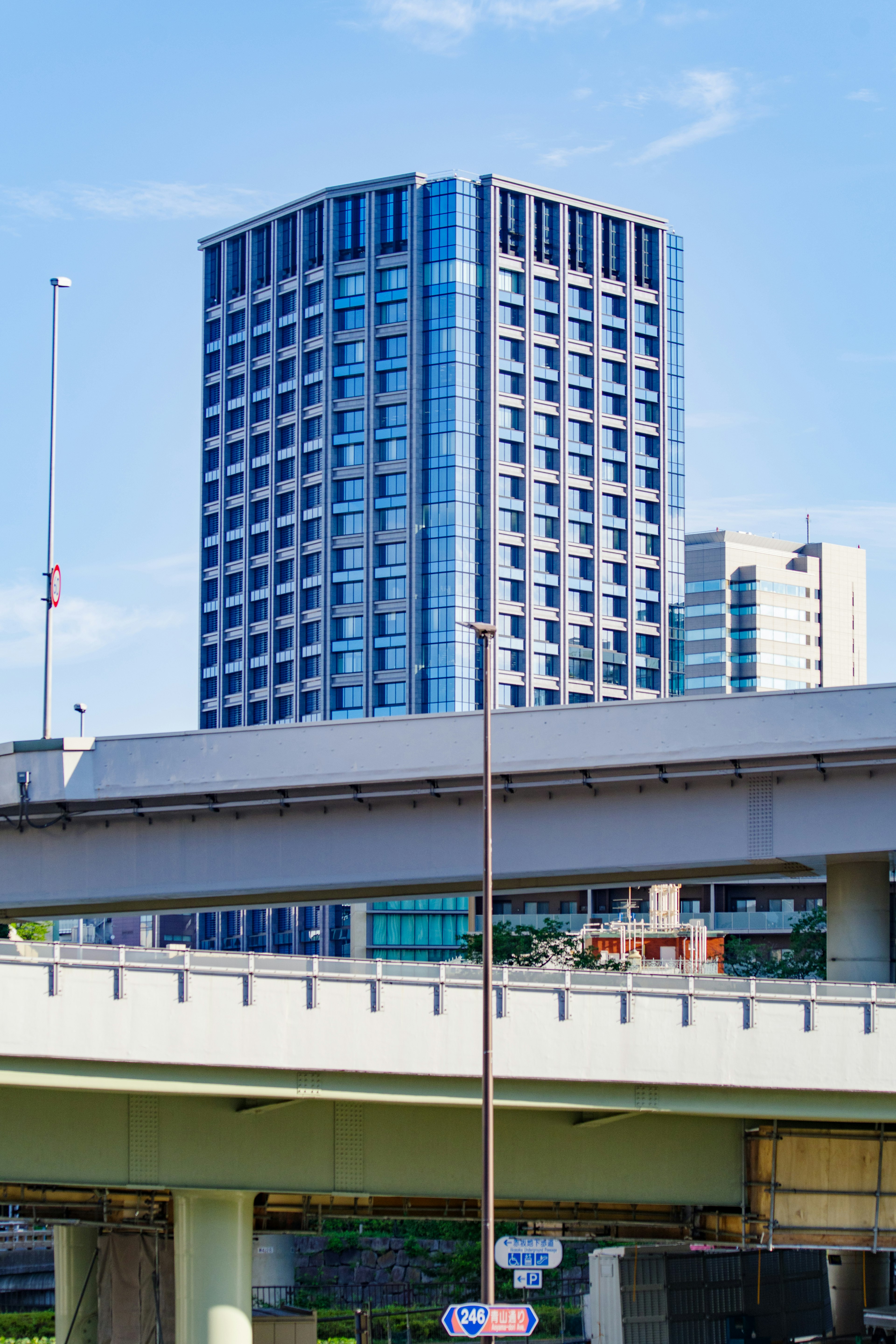 Blauer Wolkenkratzer mit moderner Architektur und Überführung im Vordergrund